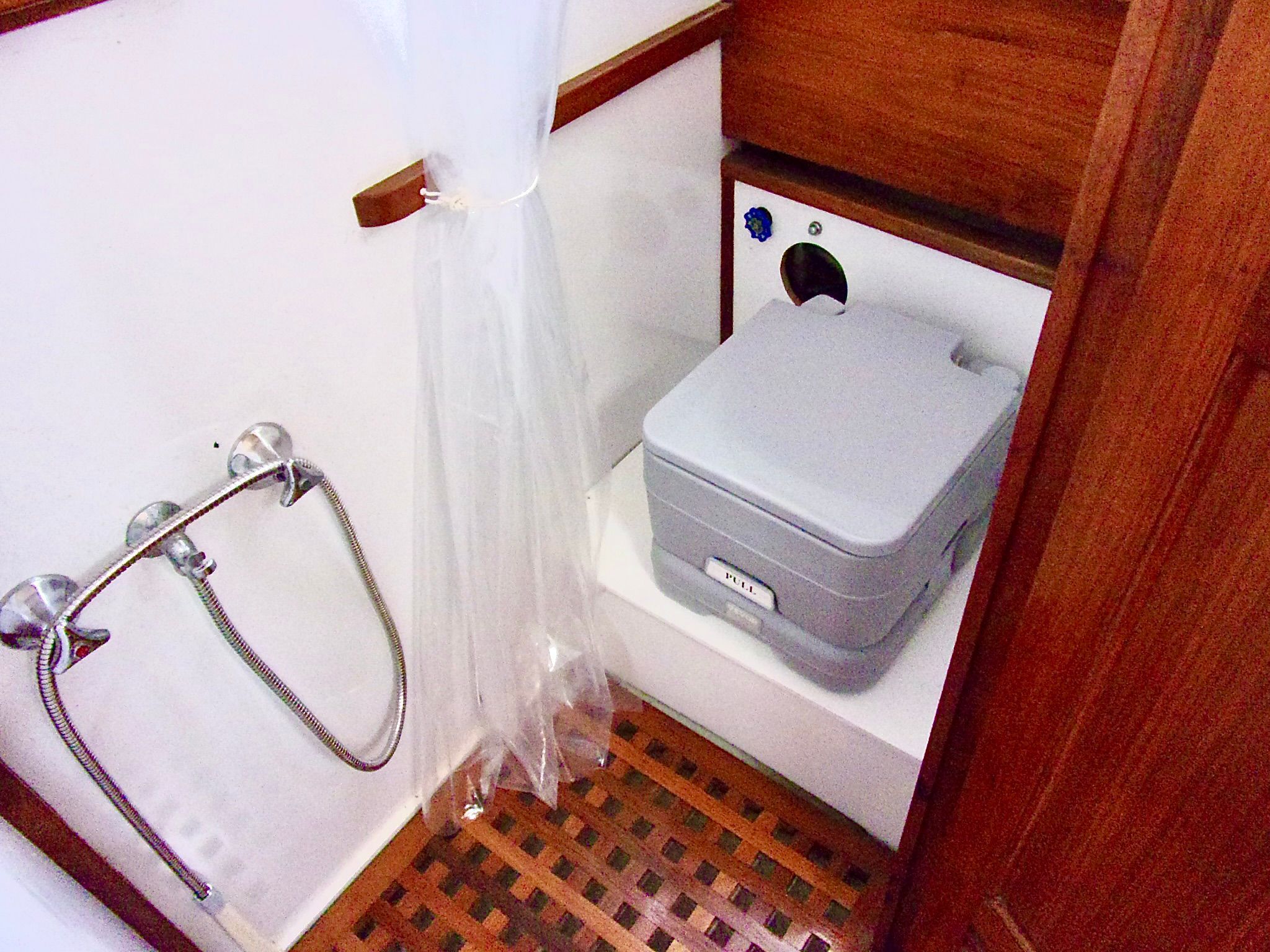 1976 CHB Trawler bathroom with portable toilet and showerhead, featuring wooden accents.