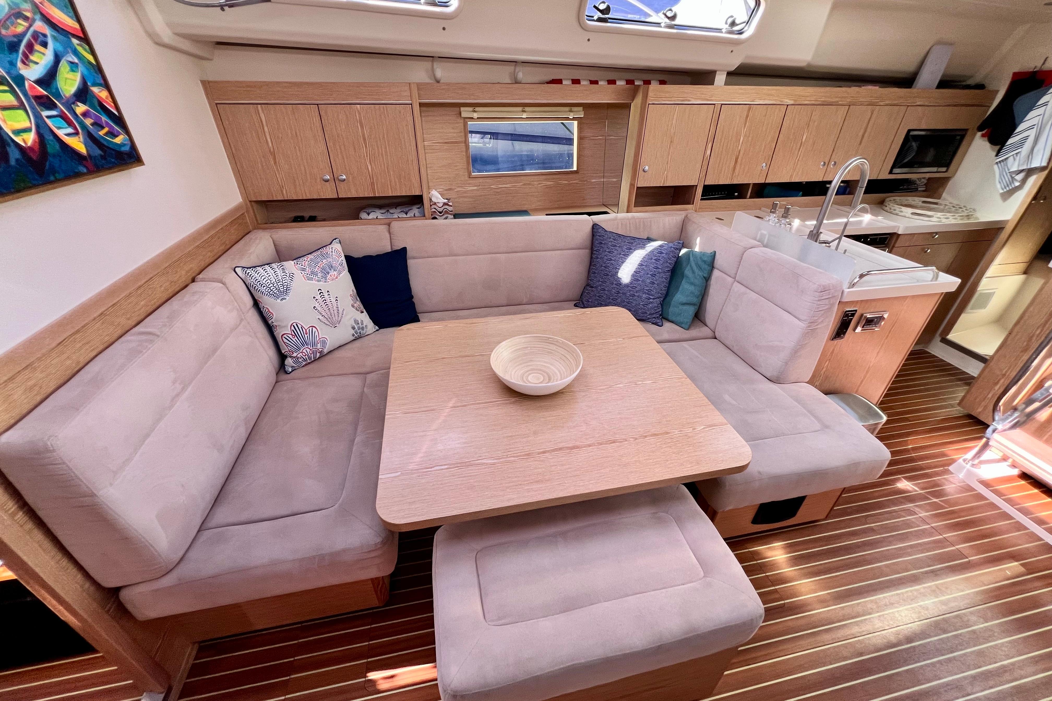 Interior of 2016 Hanse 455 yacht with cozy seating, wooden table, and modern kitchen.