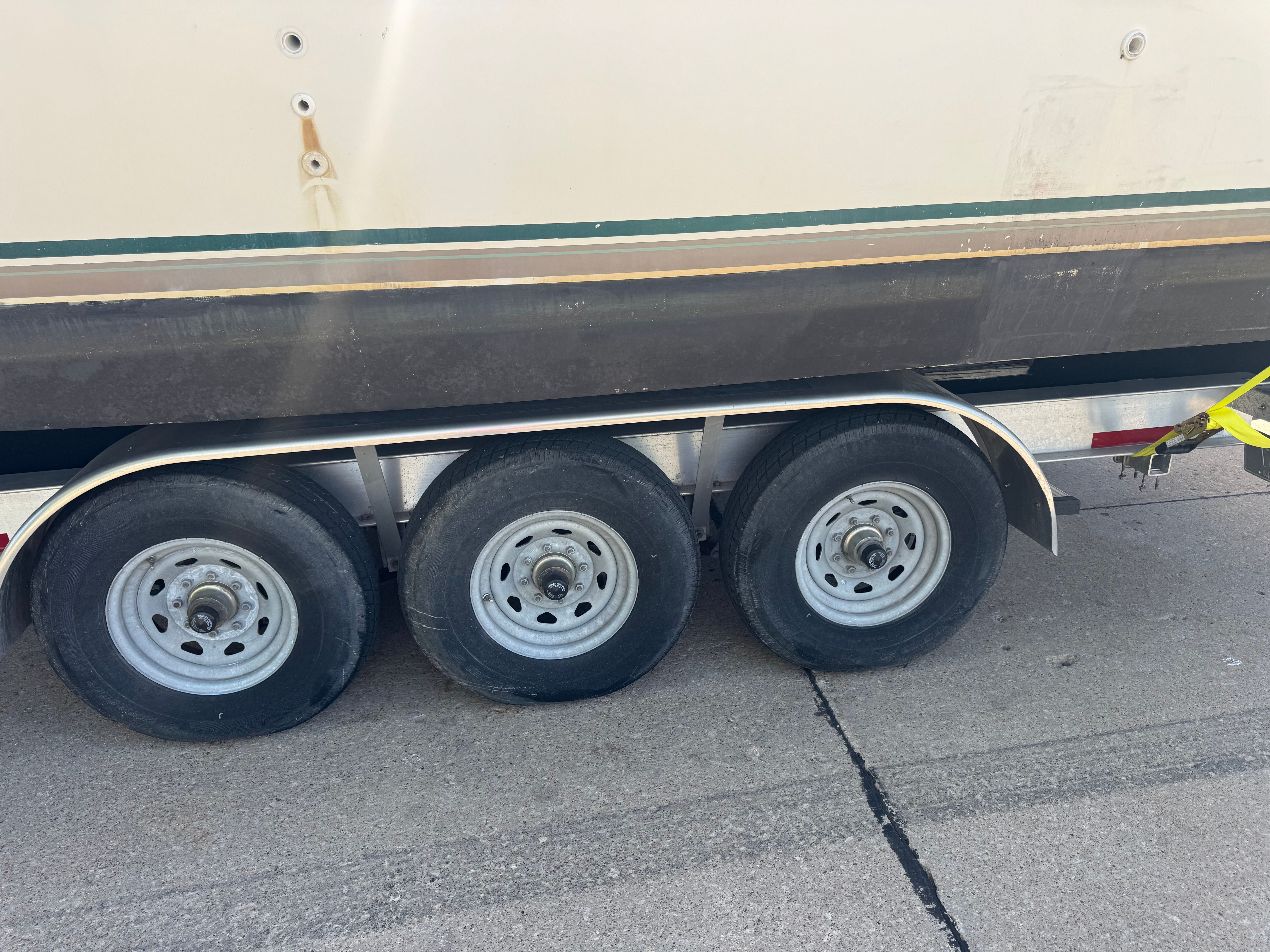 A boat on a trailer with three wheels, partially visible, parked on a road.