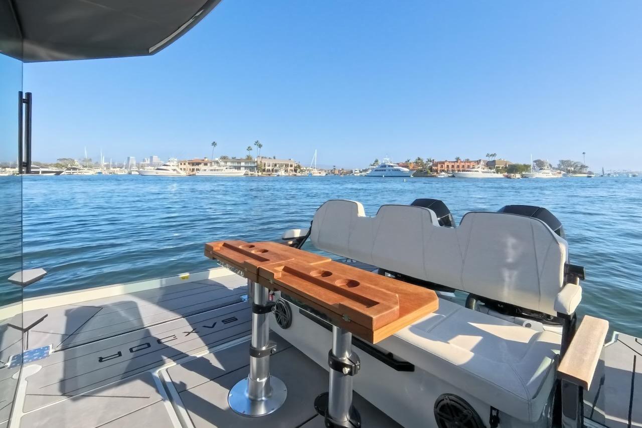 2024 Saxdor 320 GTC boat interior with seating and table, overlooking a scenic waterfront.