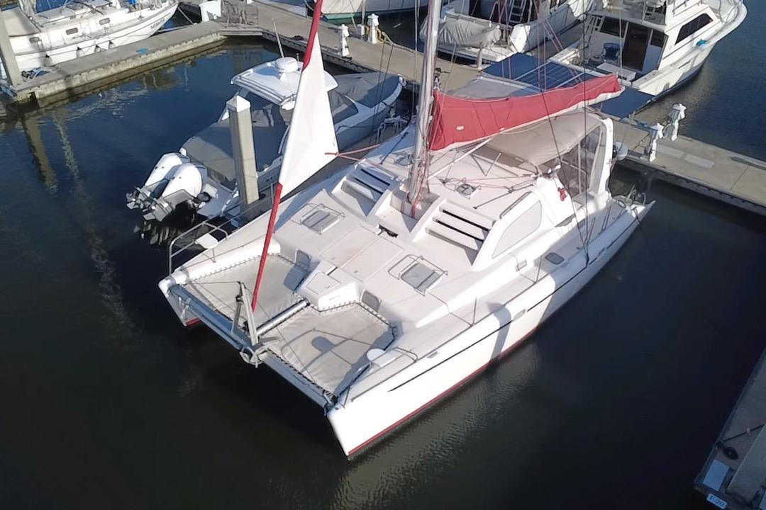 2000 Leopard 38 catamaran docked at marina with red sail and white hull.