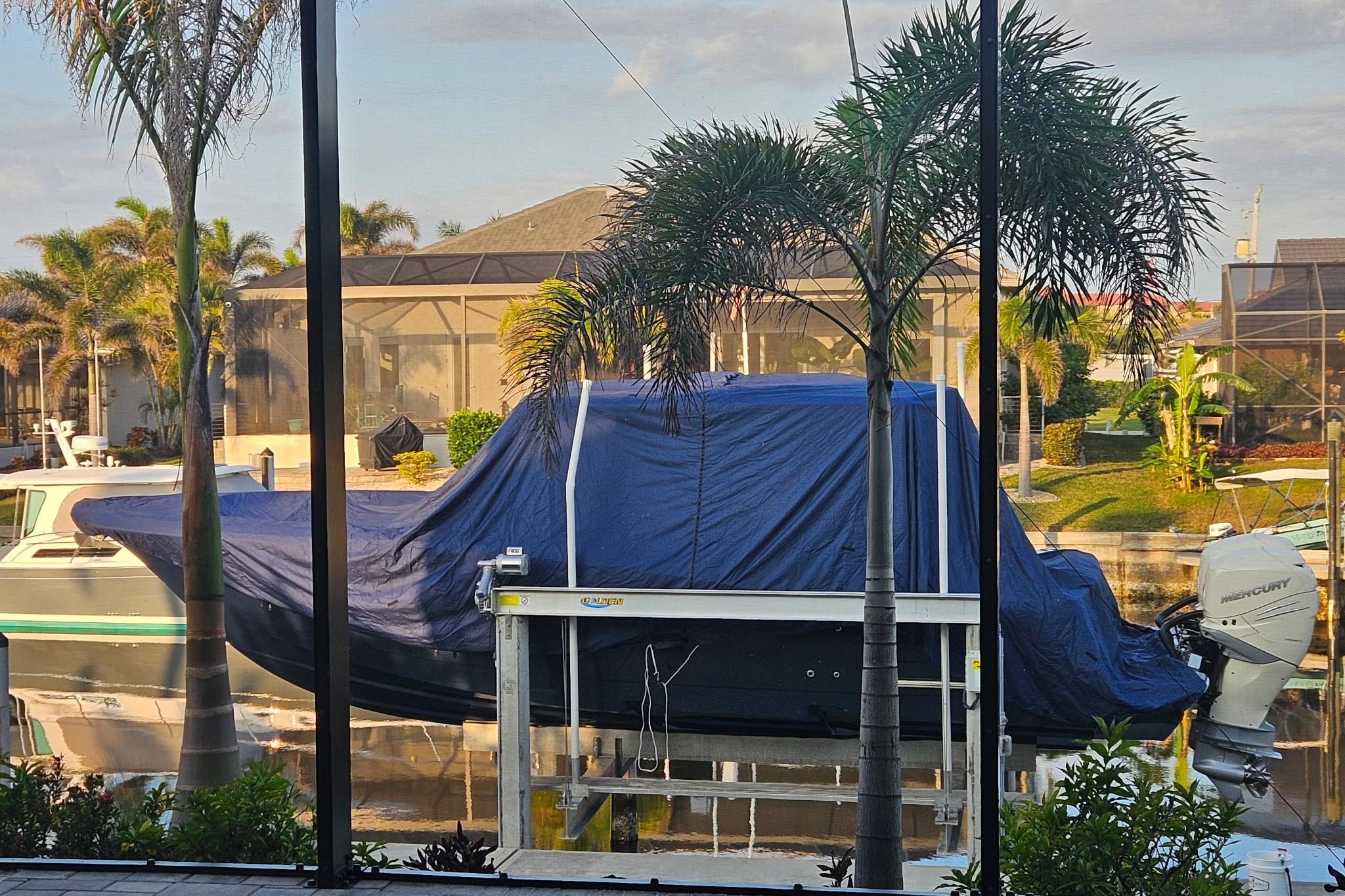 2021 Scout 330 LXF boat covered, docked near palm trees in a residential area.