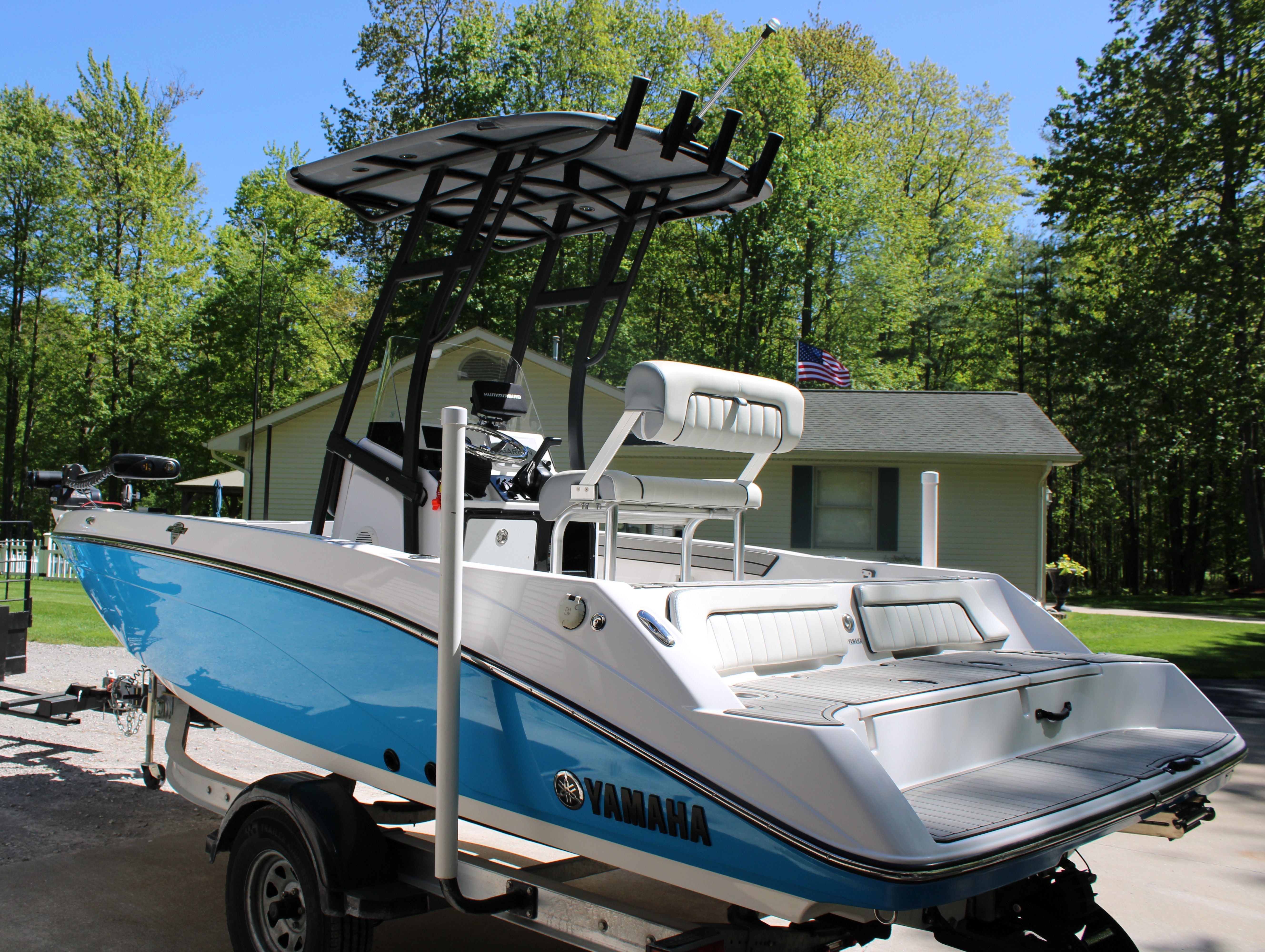 A blue and white Yamaha boat on a trailer in a wooded residential area.