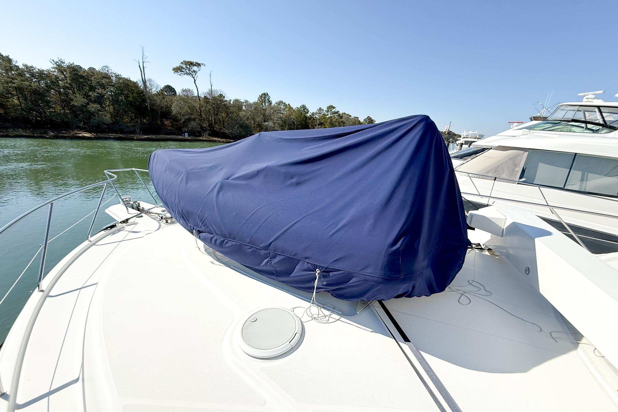 2004 Silverton 48 Convertible yacht with blue cover on deck, docked near trees.