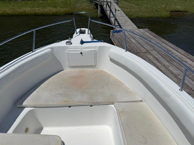 The image shows the bow of a 1999 Aquasport 215 DC boat docked at a wooden pier.