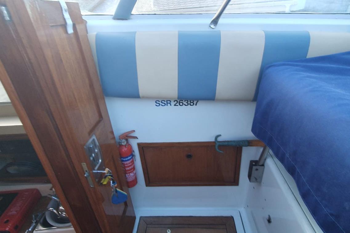 Interior of 1989 Fairey Spearfish MKIII boat with wooden door, fire extinguisher, and blue-striped upholstery.
