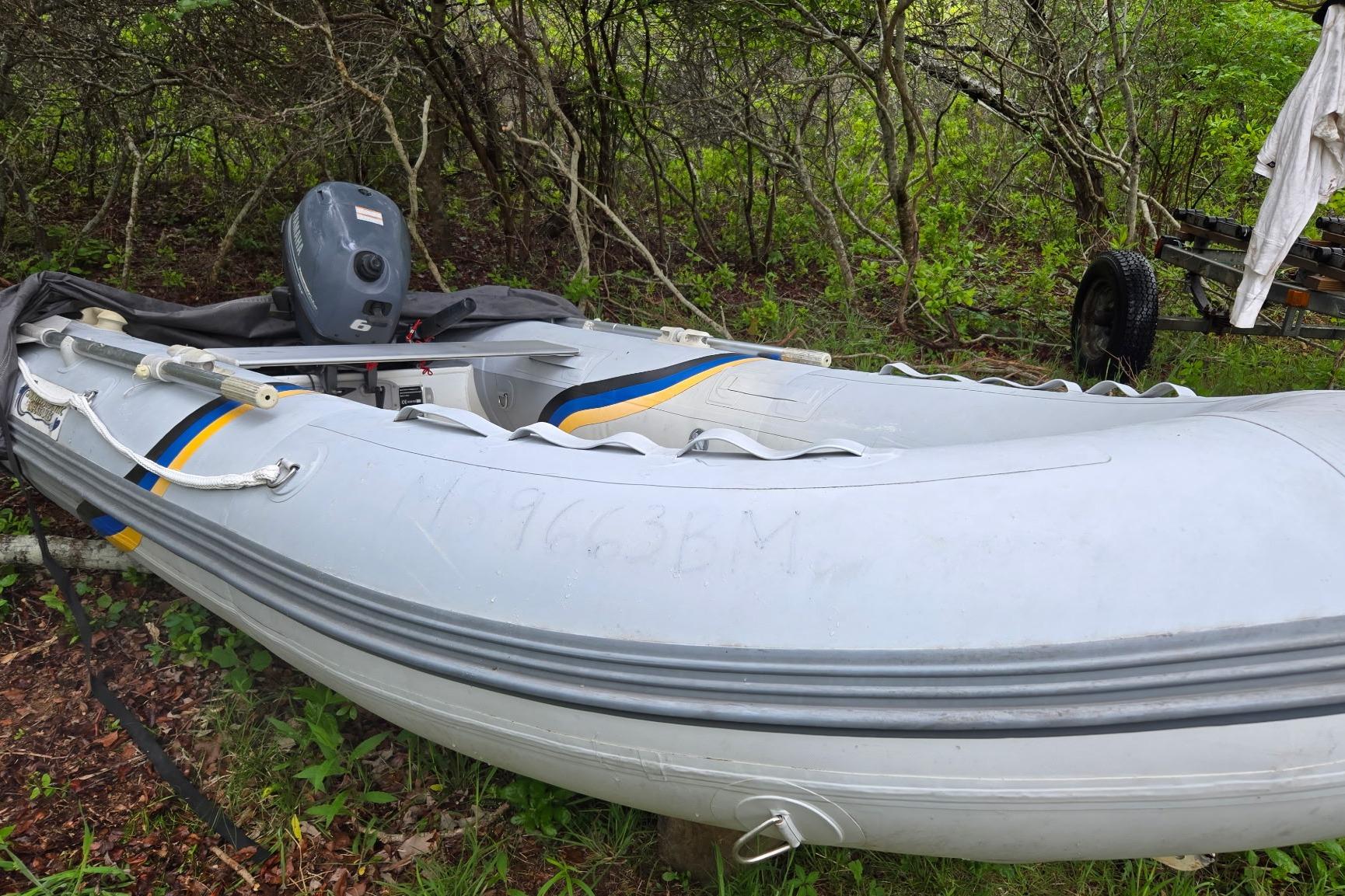Inflatable boat with outboard motor, parked on grass, surrounded by trees.
