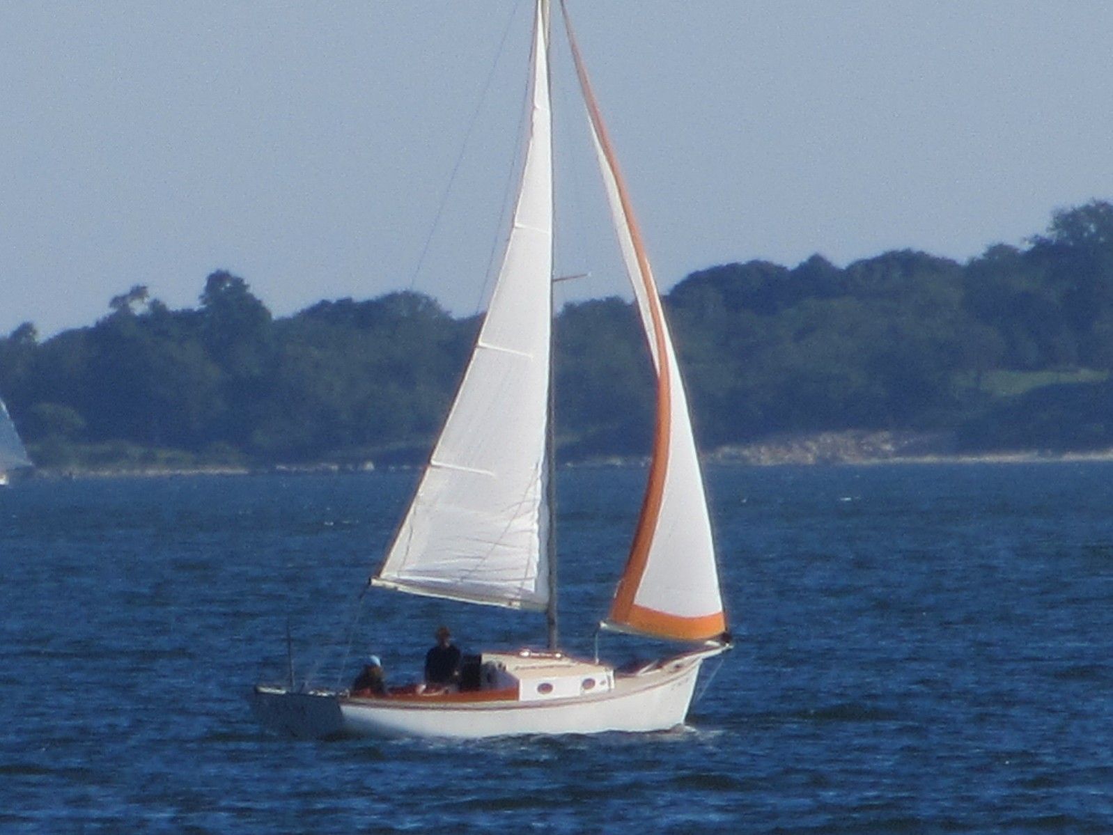 A sailboat with white sails and an orange stripe sails on calm water.