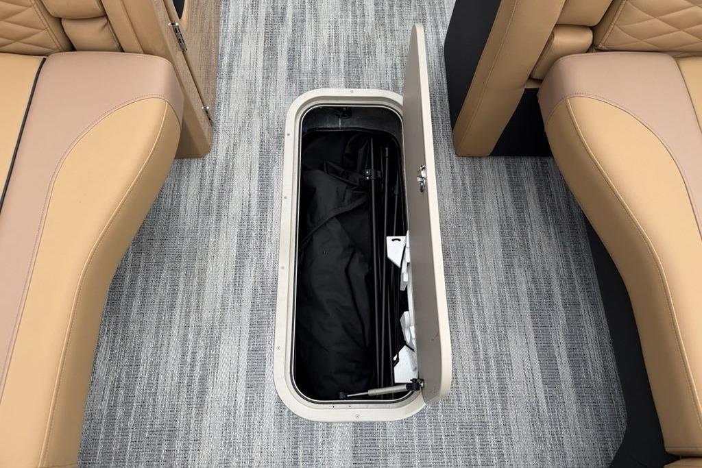 Open storage compartment on 2026 Godfrey Monaco 235 SFLC iMPACT boat, between tan seats.