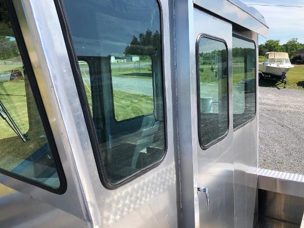 A modern workboat with large windows and sturdy metal frame, parked on a gravel lot.