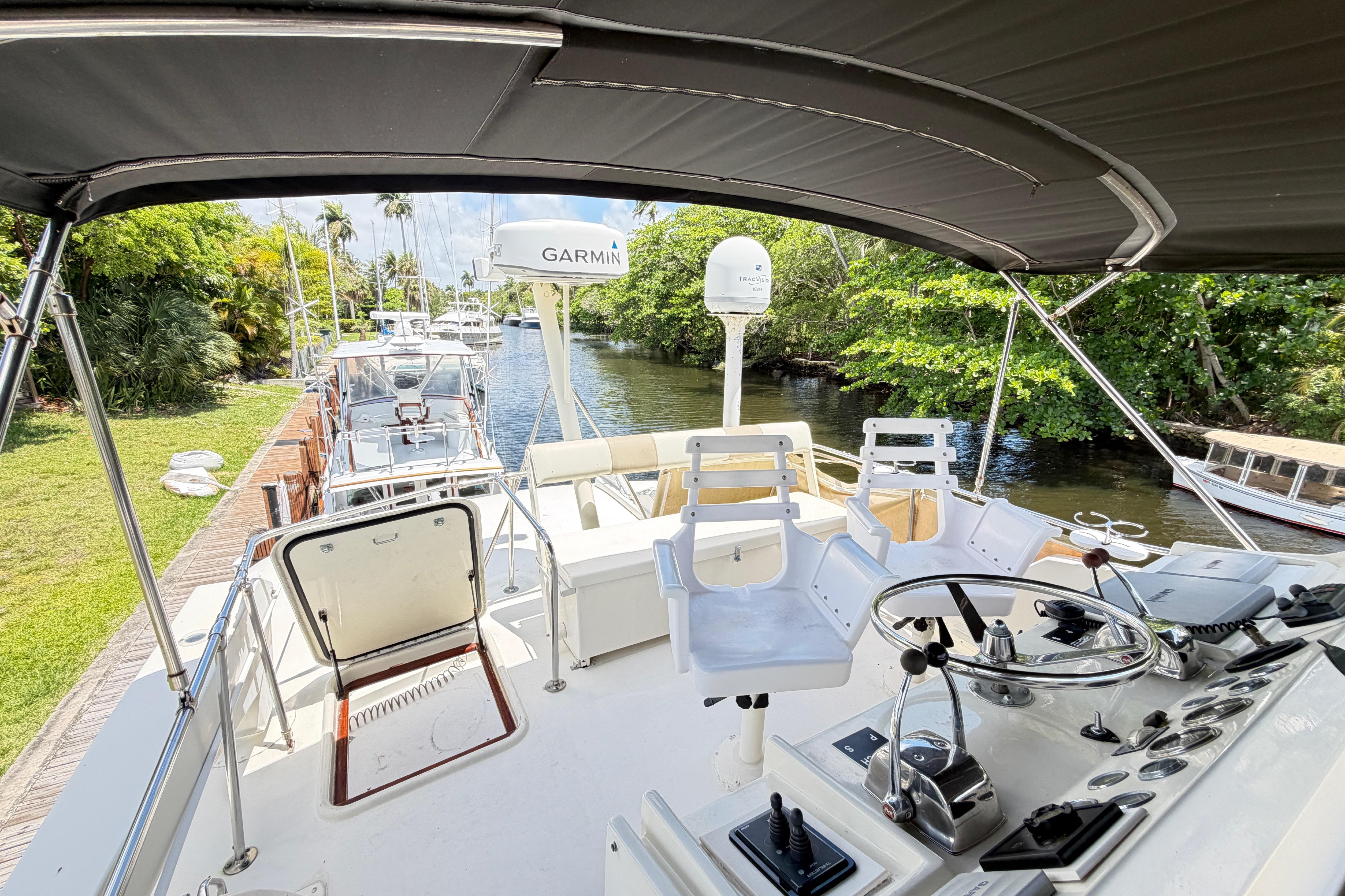 1978 Hatteras 53 Motor Yacht helm with Garmin equipment, docked by lush greenery.