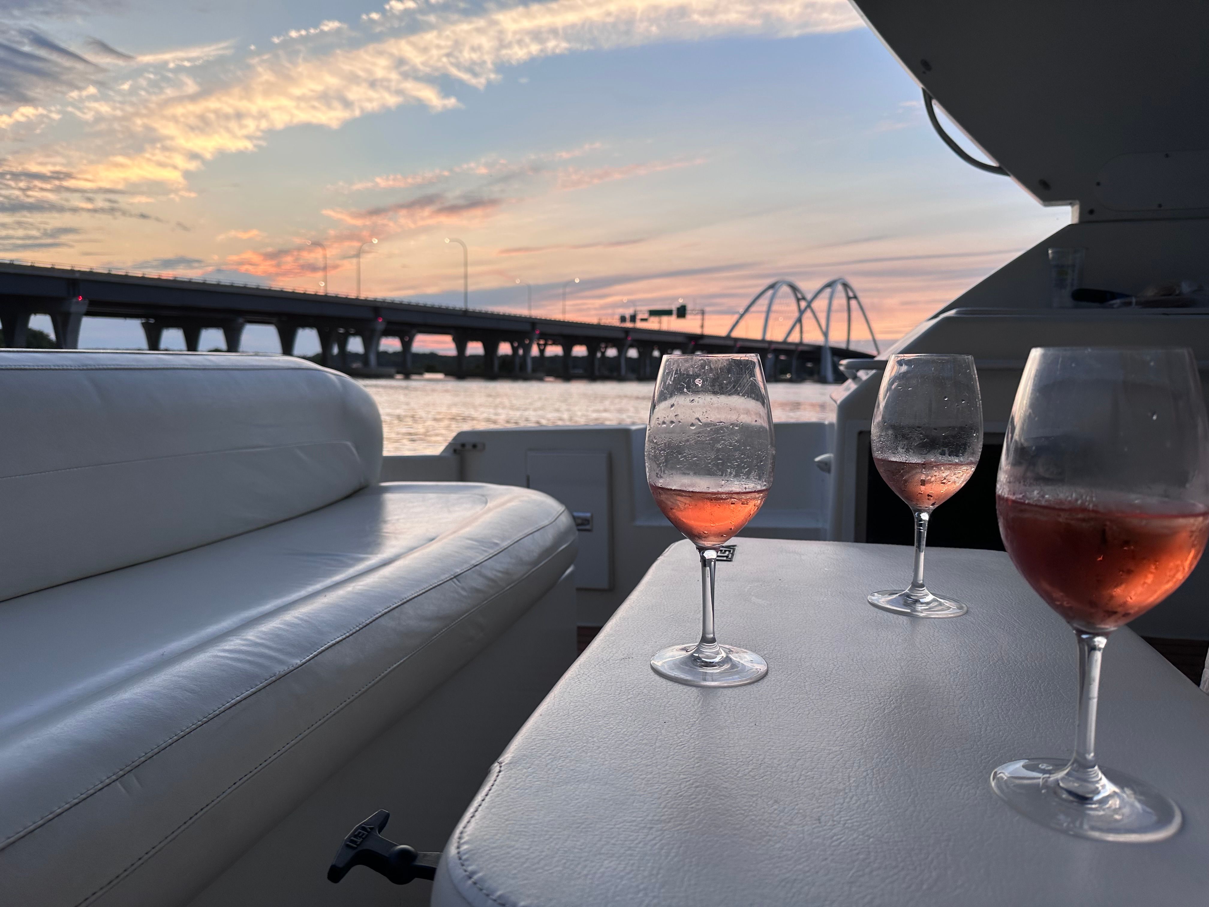 Three wine glasses on a boat table at sunset, with a bridge in the background.