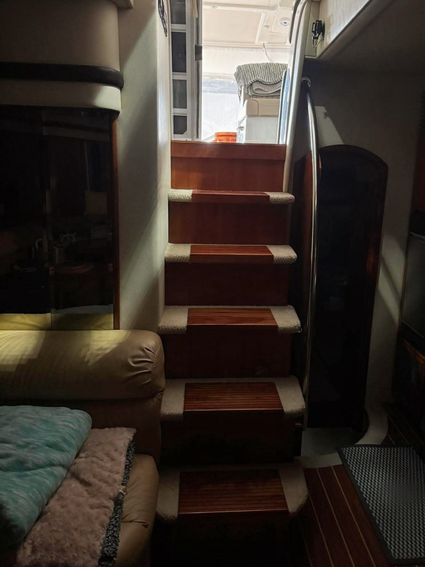 Interior view of a yacht with stairs leading to the upper deck. Padded seating and wooden floors visible.
