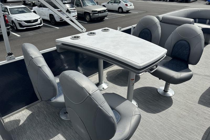 2022 Bennington L 23 L-Bench boat interior with gray seating and table in a parking lot.