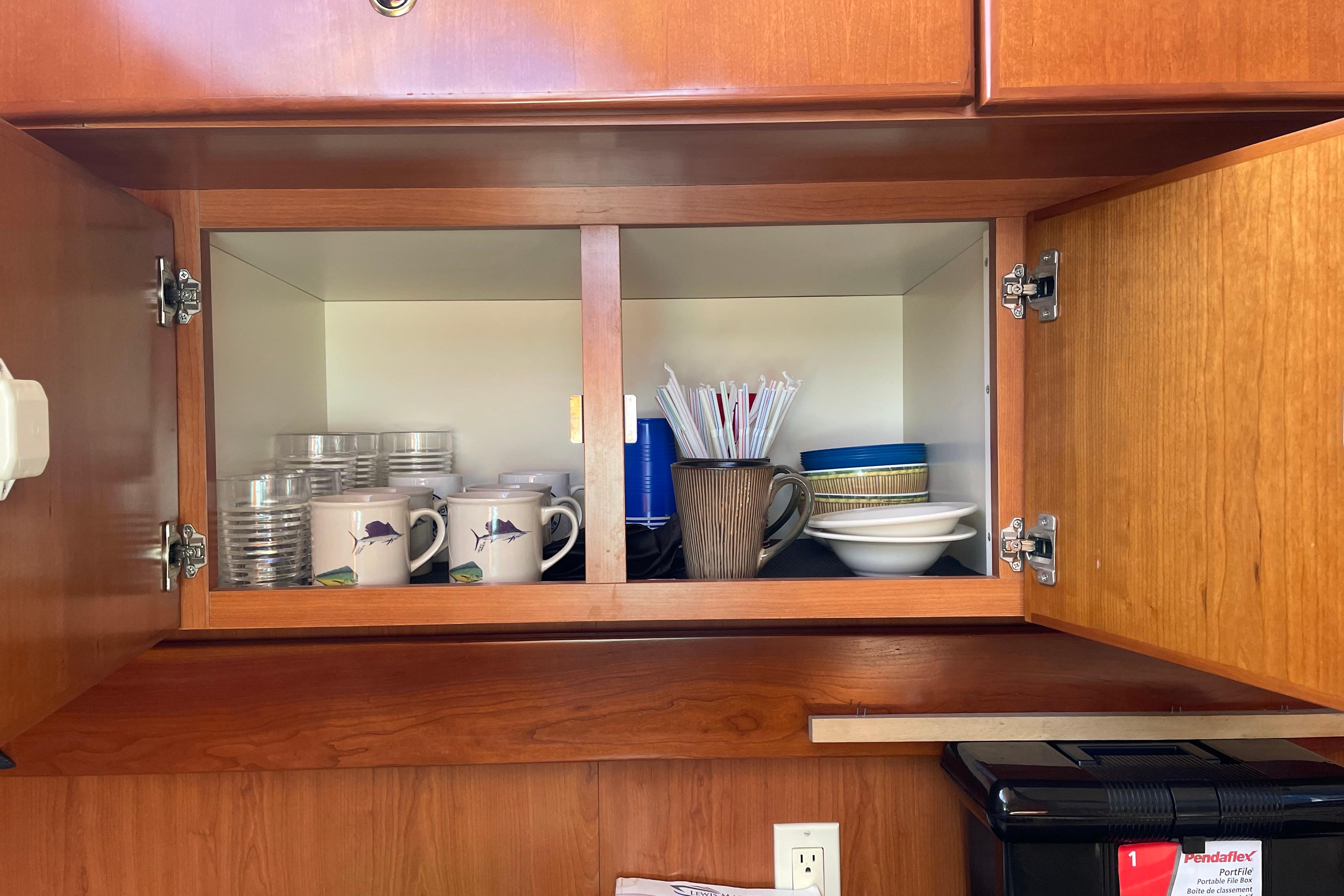 Open wooden cabinet in 2007 Silverton 42 Convertible, displaying mugs, bowls, and straws.