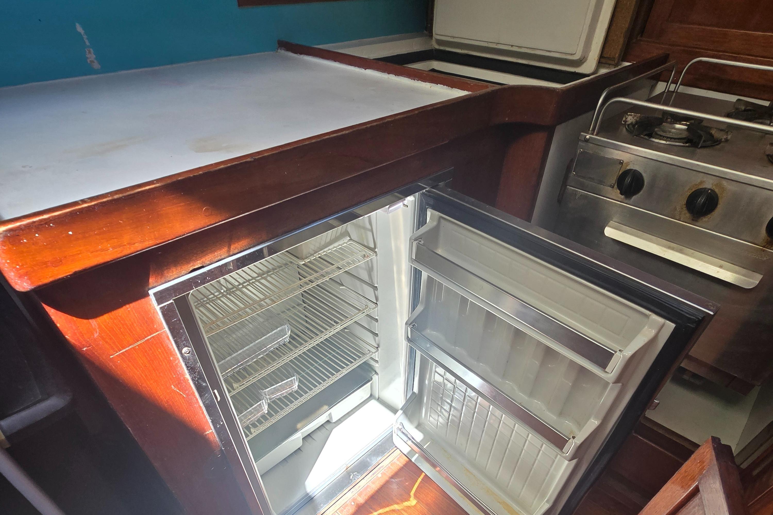 Interior of a 1978 Herreshoff 50 yacht kitchen with open fridge and stove.