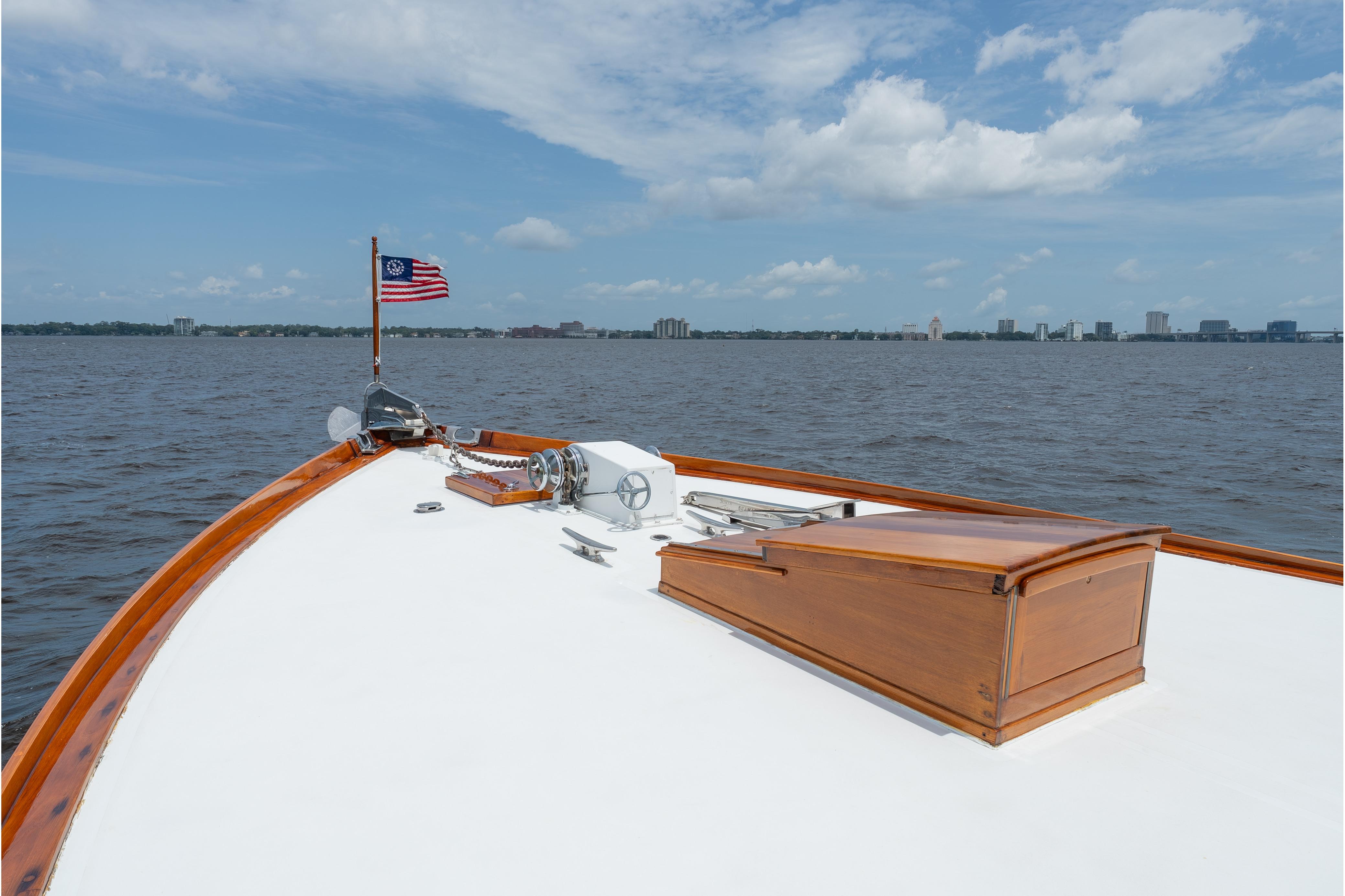 Bow of a 1963 Trumpy Classic yacht with American flag, overlooking a city skyline.