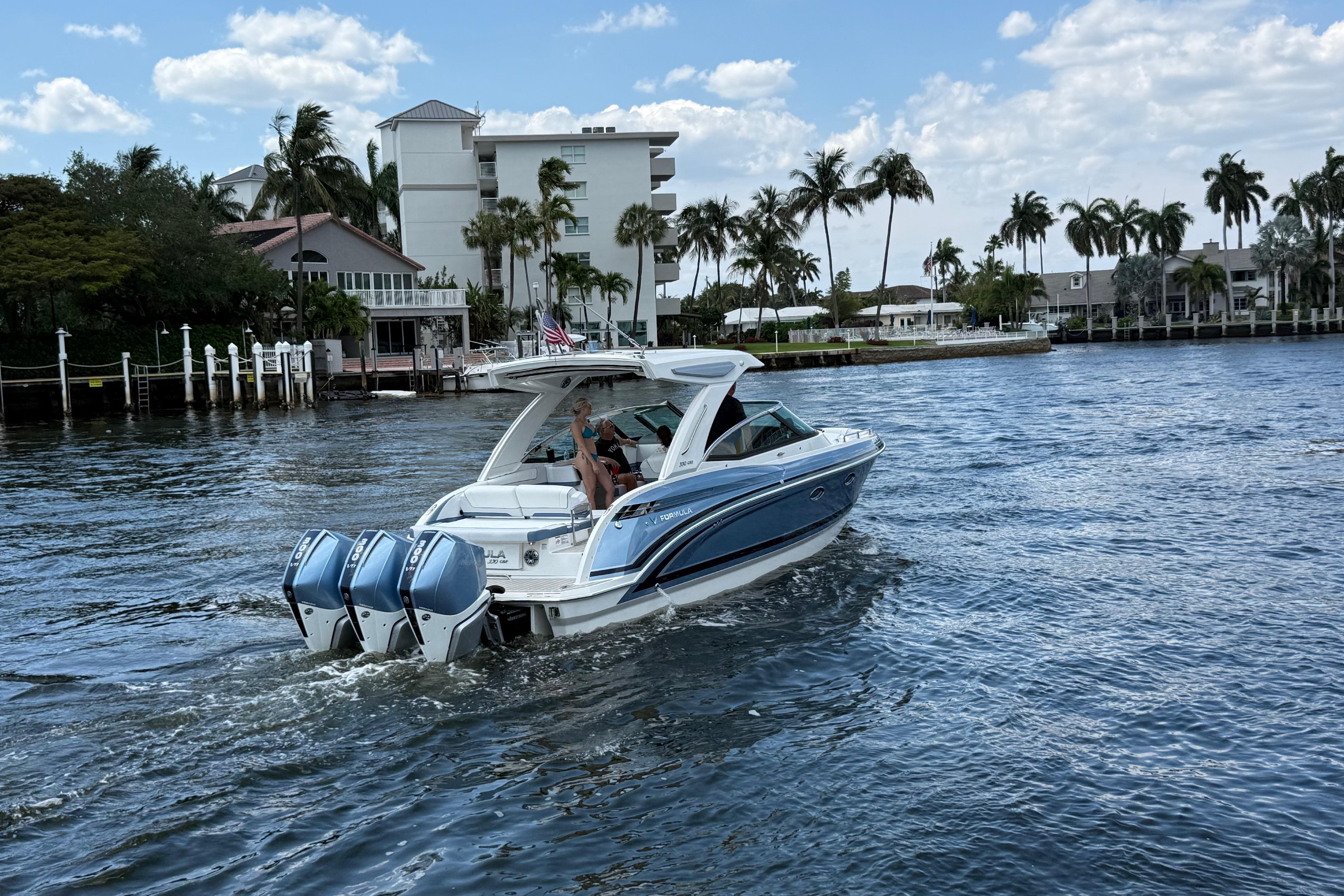 2025 Formula 330 Crossover Bowrider OB cruising on a scenic waterway with palm trees.