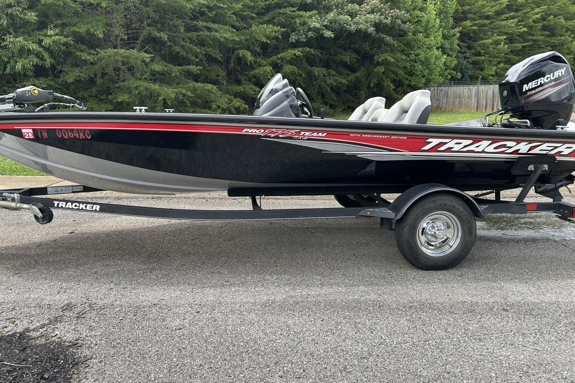 2022 Tracker Pro Team 175 TF boat on trailer, parked on asphalt, surrounded by trees.