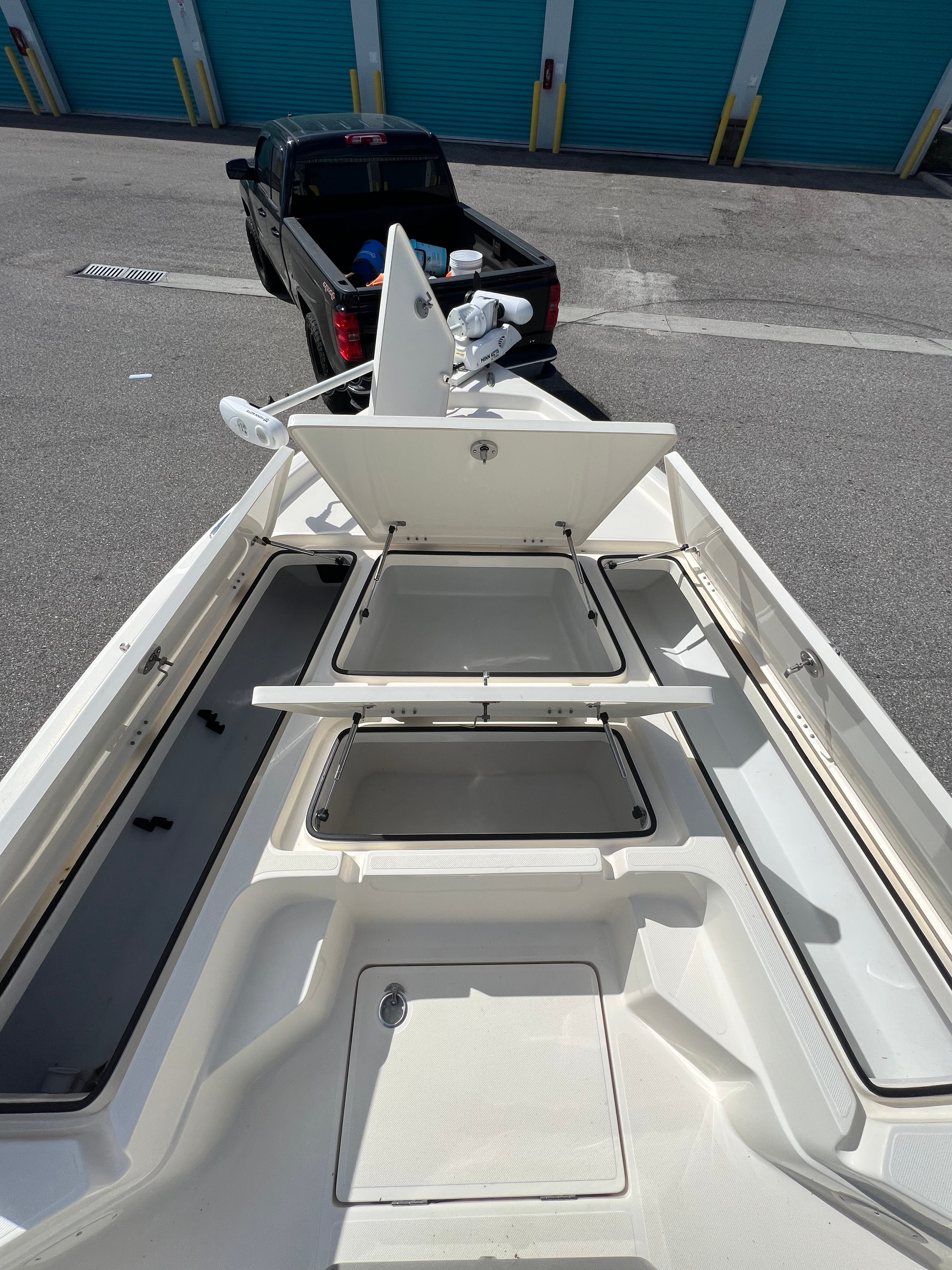 View of a Skeeter SX240 boat deck with open storage compartments and a parked truck in the background.