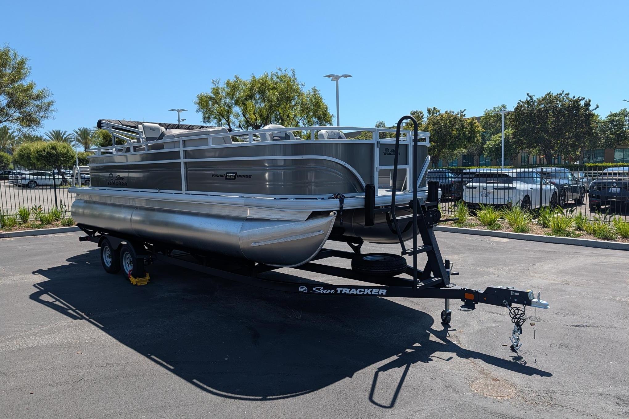 2026 Sun Tracker Fishin' Barge 22 DLX pontoon boat on trailer in parking lot.