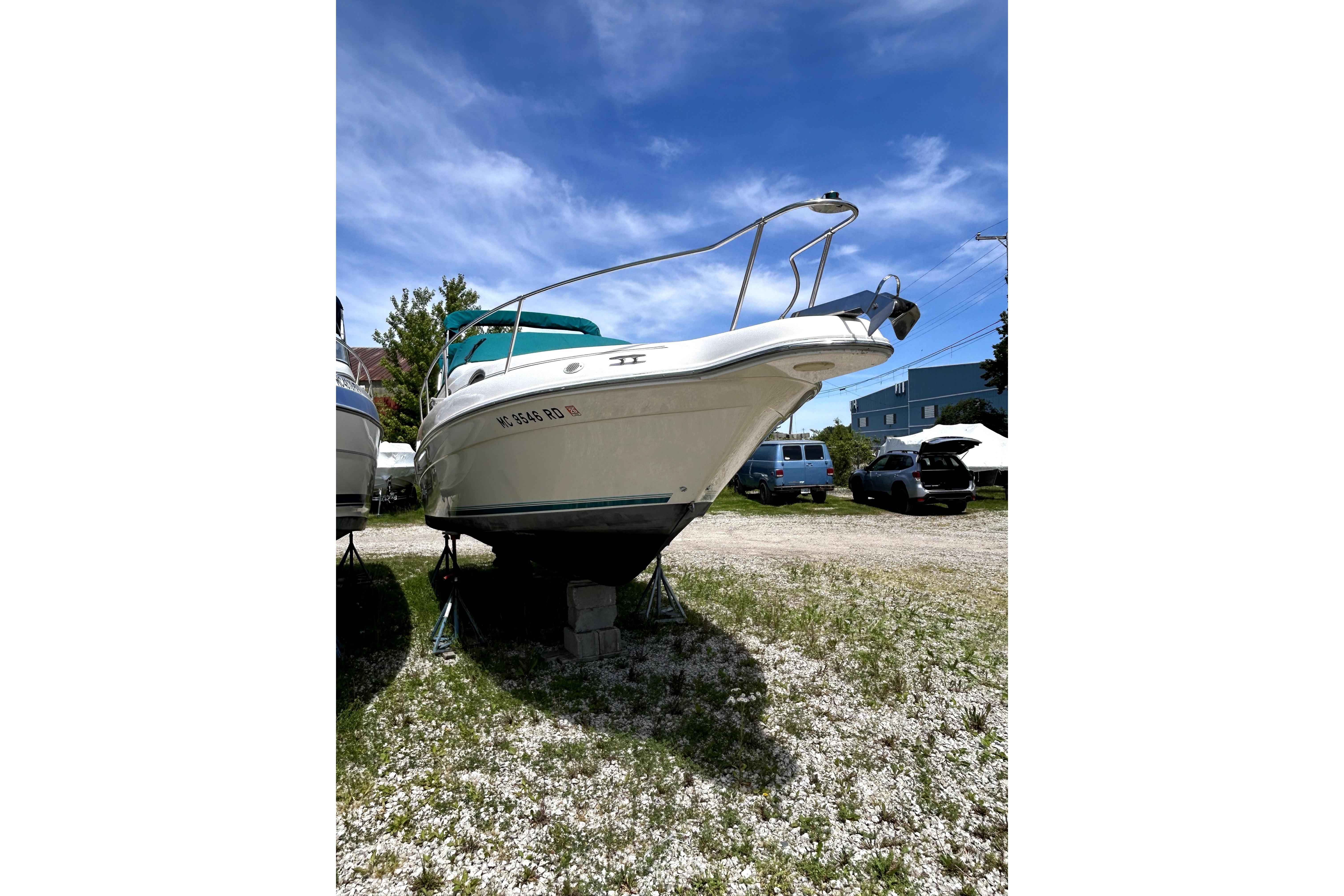 1995 Sea Ray 250 Sundancer boat on stands, parked outdoors under a clear blue sky.