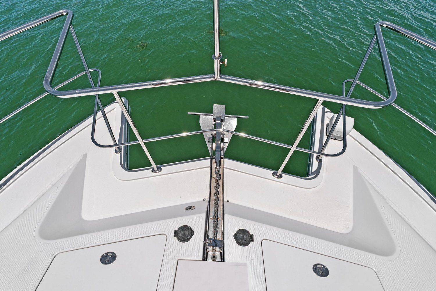 Bow of a catamaran with stainless steel railing and anchor over green water.