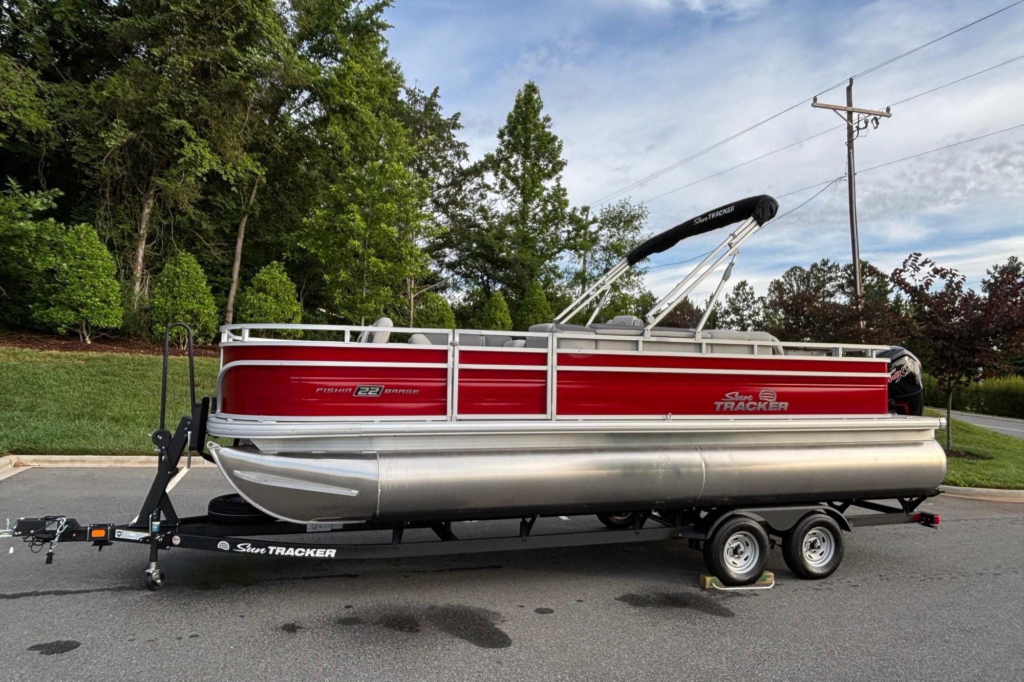 2026 Sun Tracker Fishin' Barge 22 DLX pontoon boat on trailer, parked outdoors.