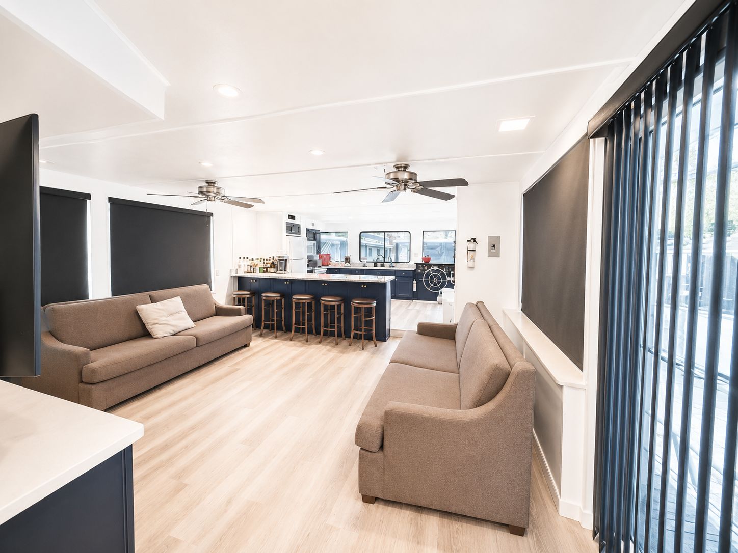 Interior of a houseboat with sofas, a bar counter, and windows.