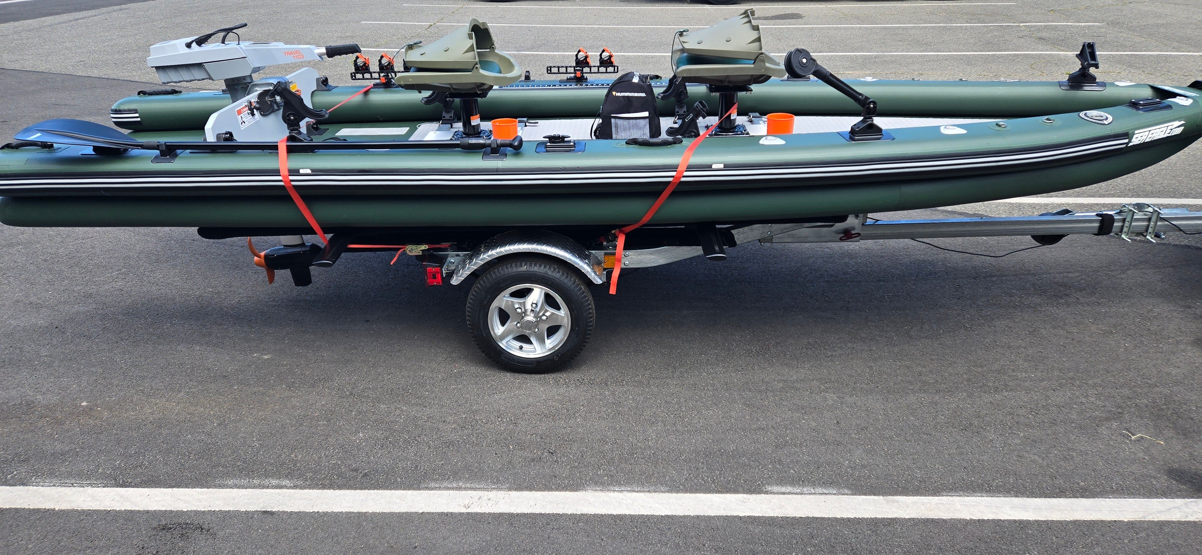 A green inflatable boat on a trailer, equipped with motors and accessories.
