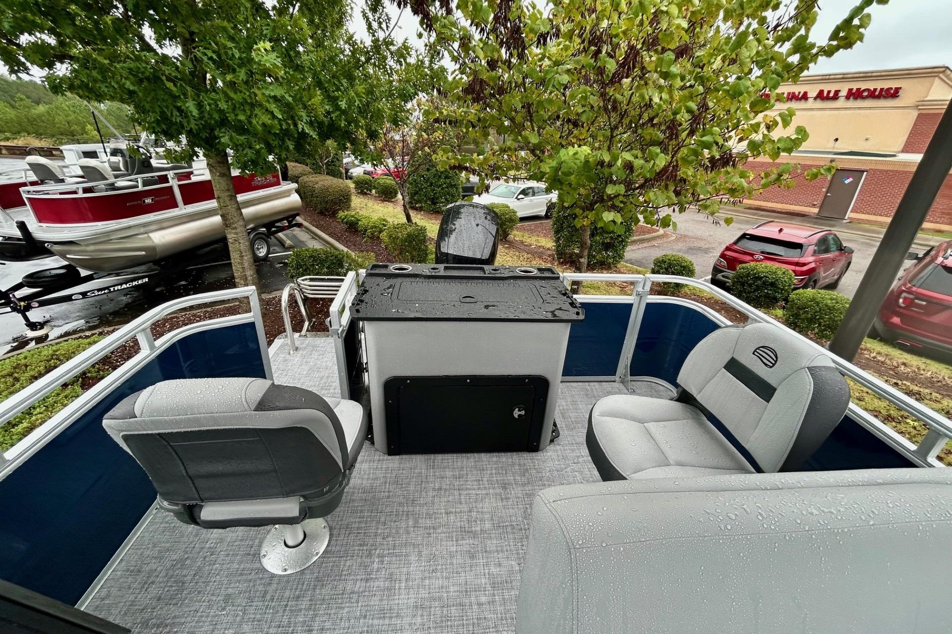 2026 Sun Tracker SportFish 22 DLX pontoon boat interior with seating and console, parked outdoors.