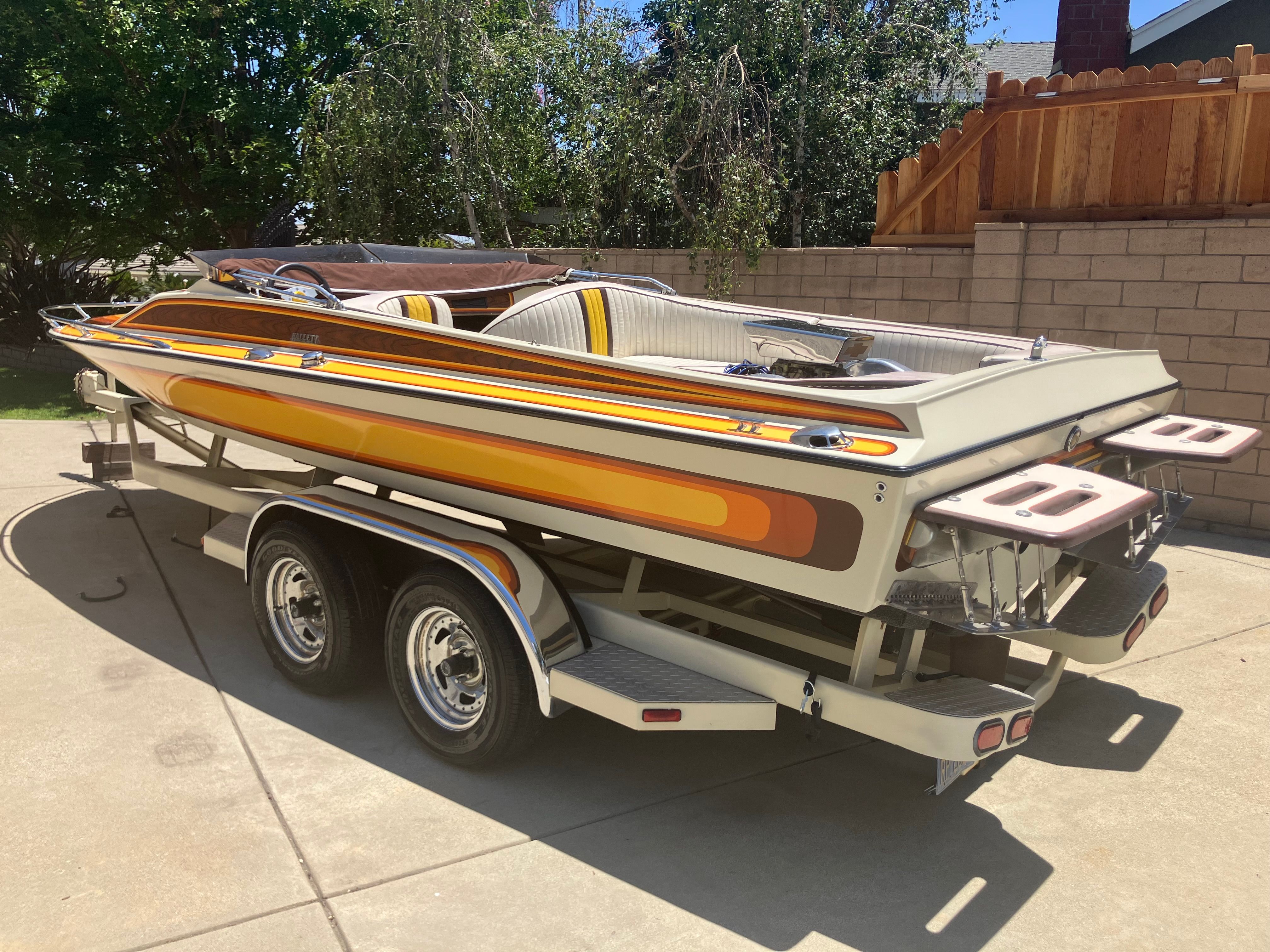 A 1982 Hallett 20’ boat with colorful stripe design sits on a trailer outdoors.