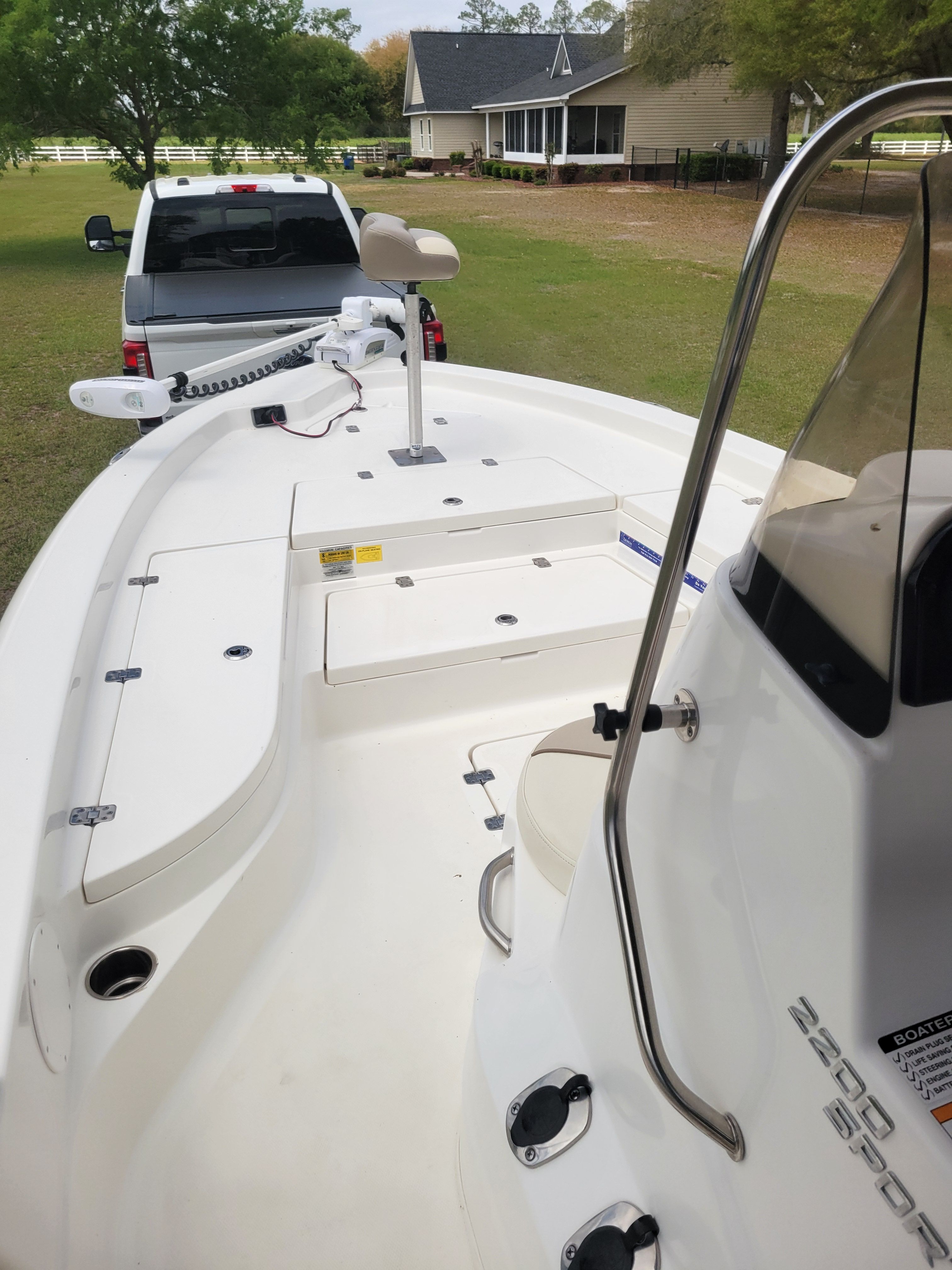 A white boat is on a trailer in front of a house on a grassy area.