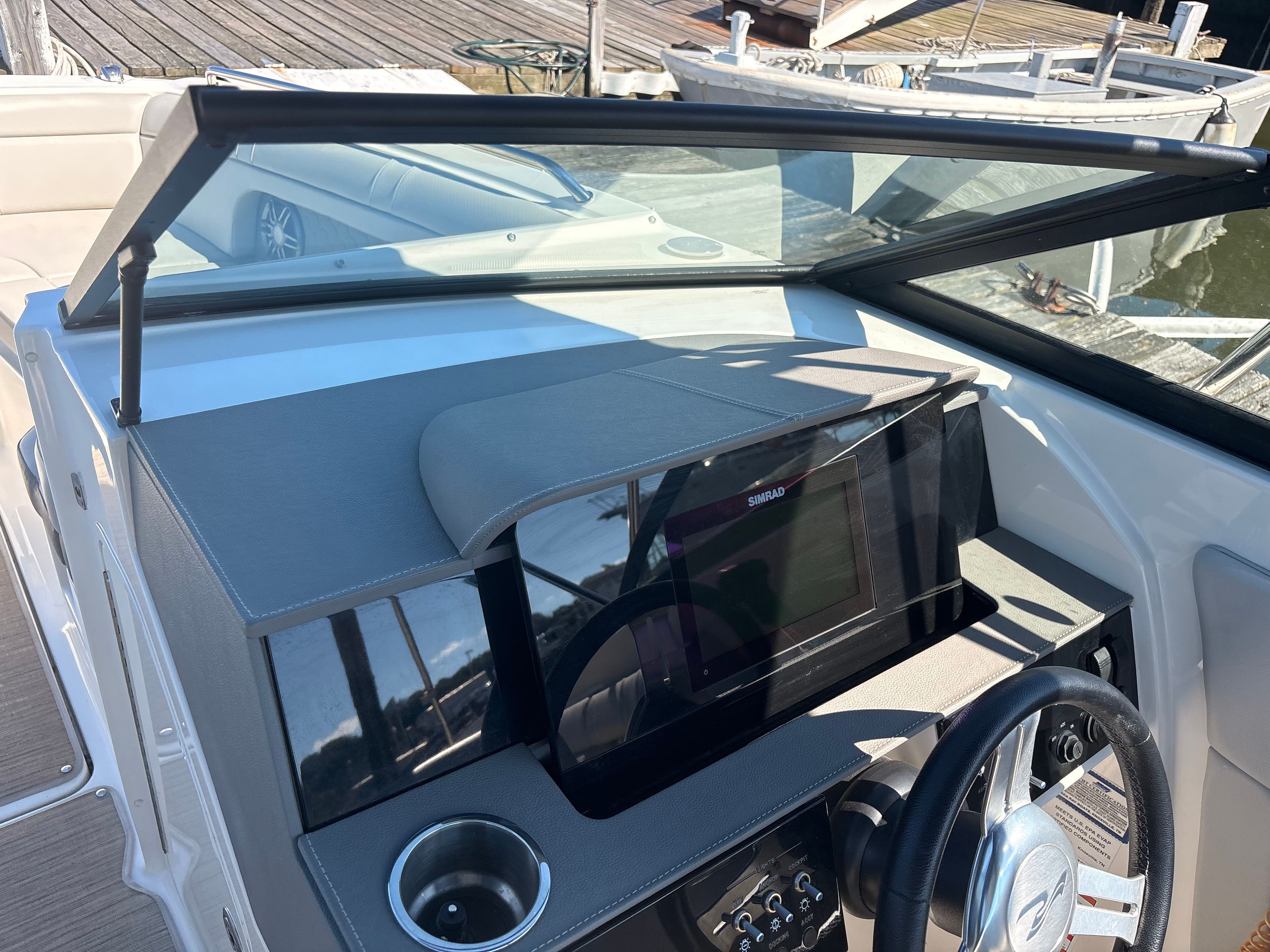 The image shows the cockpit of a 2022 Sea Ray SDX 270 Outboard. It features a modern dashboard with a large screen and steering wheel. A dock and water are visible in the background.