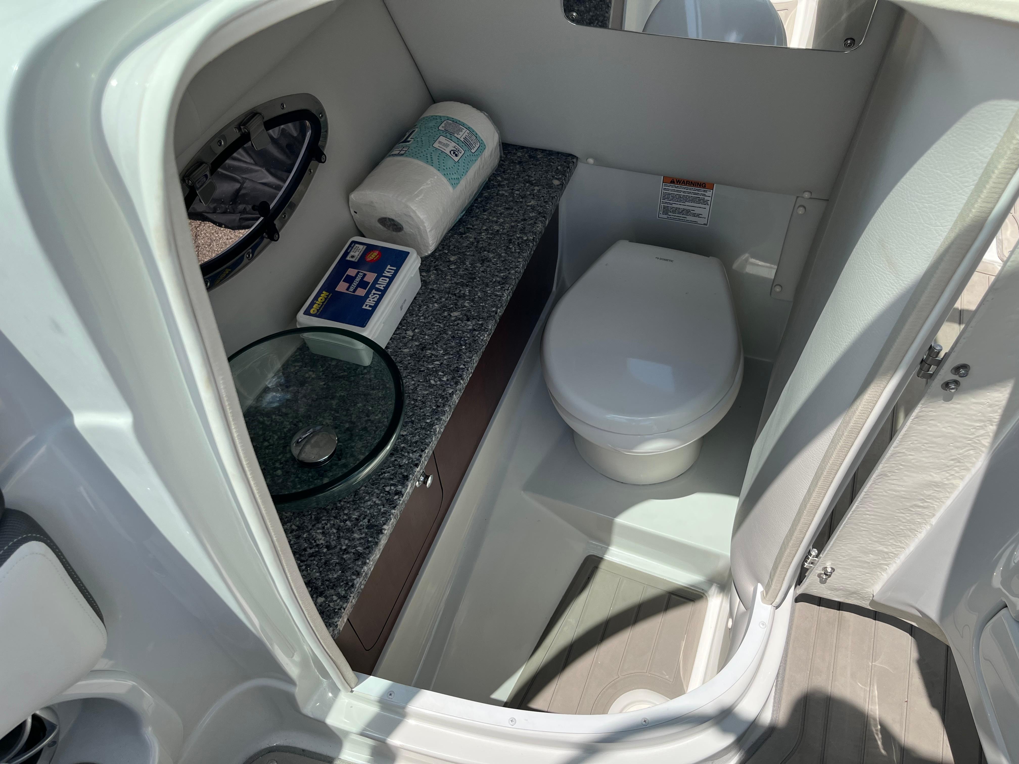 2022 Crownline 280 SS boat bathroom with toilet, sink, and storage shelf.