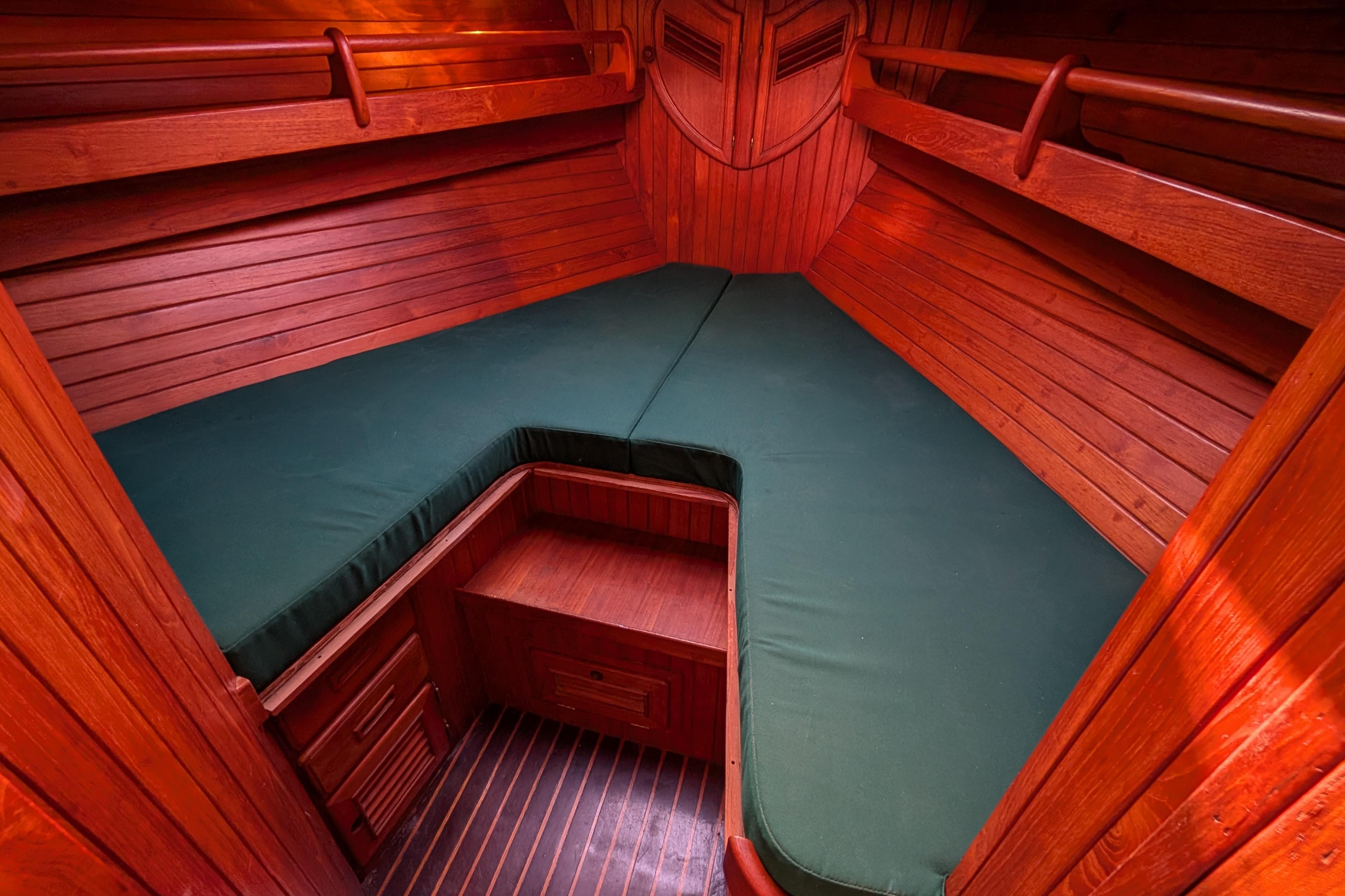 Cozy wooden cabin interior of 1983 Robert Perry 41 sailboat with green cushions.