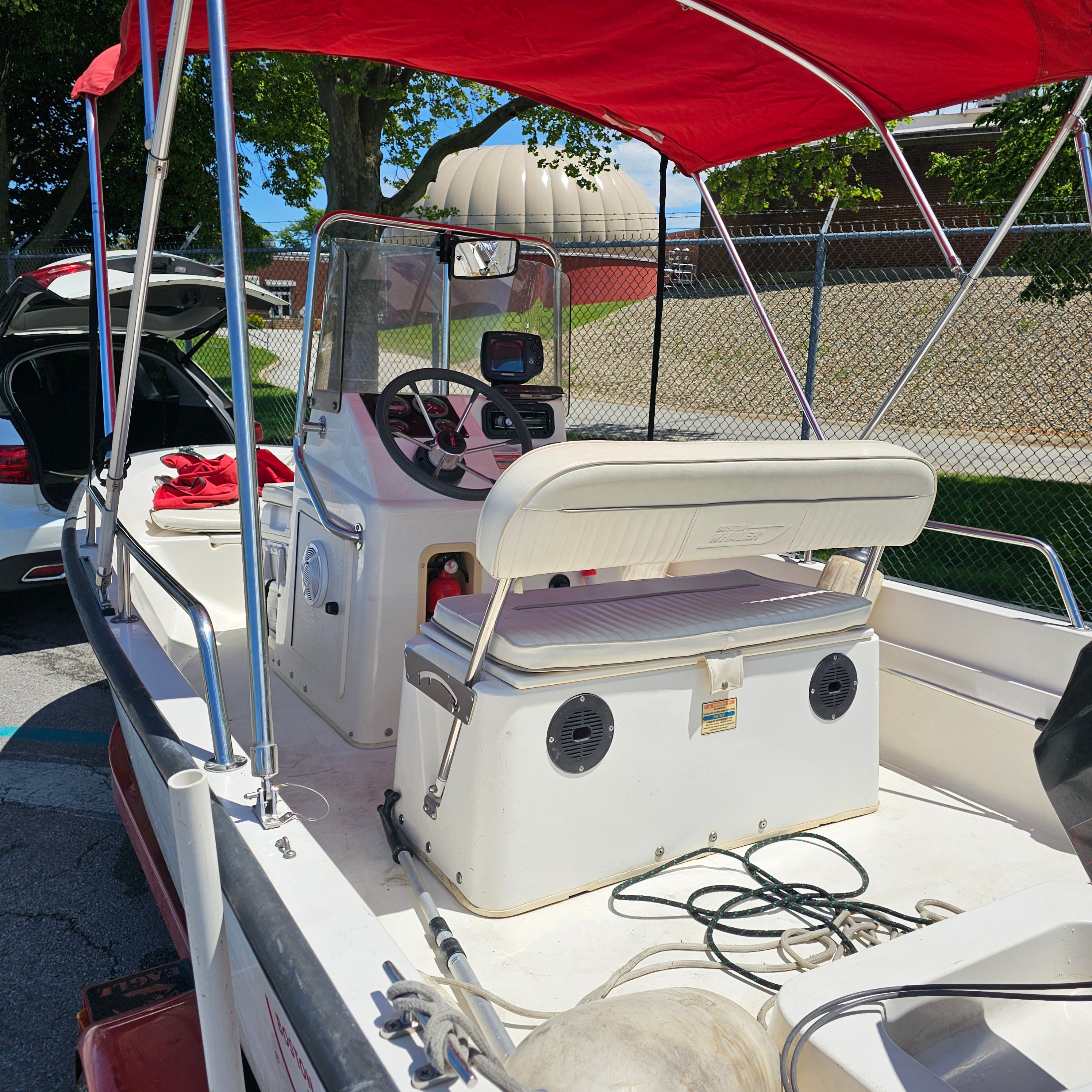 A boat with a red canopy and white seating area, parked next to a car.