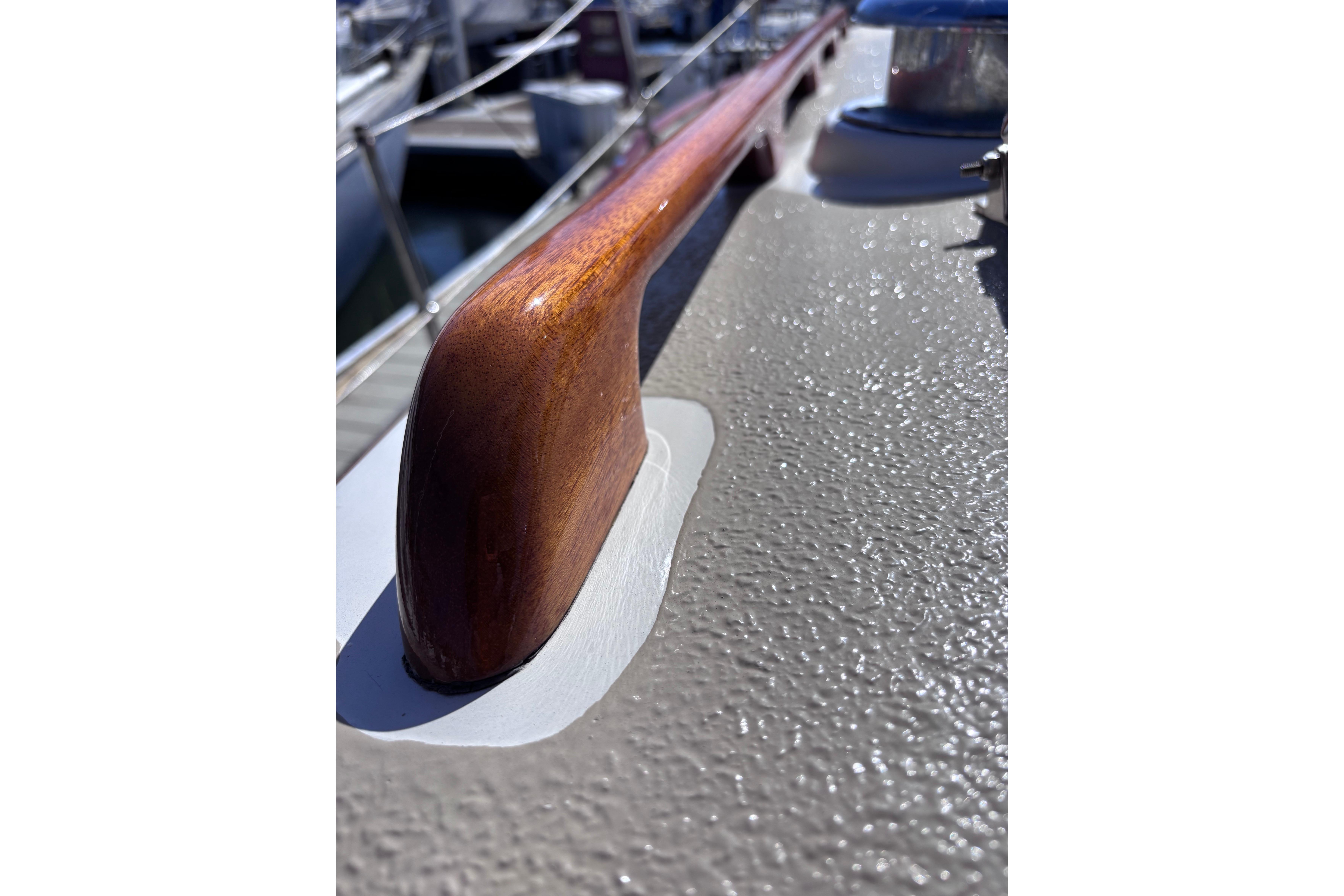 Close-up of a 1978 Swift 33 boat's polished wooden handrail and textured deck surface.