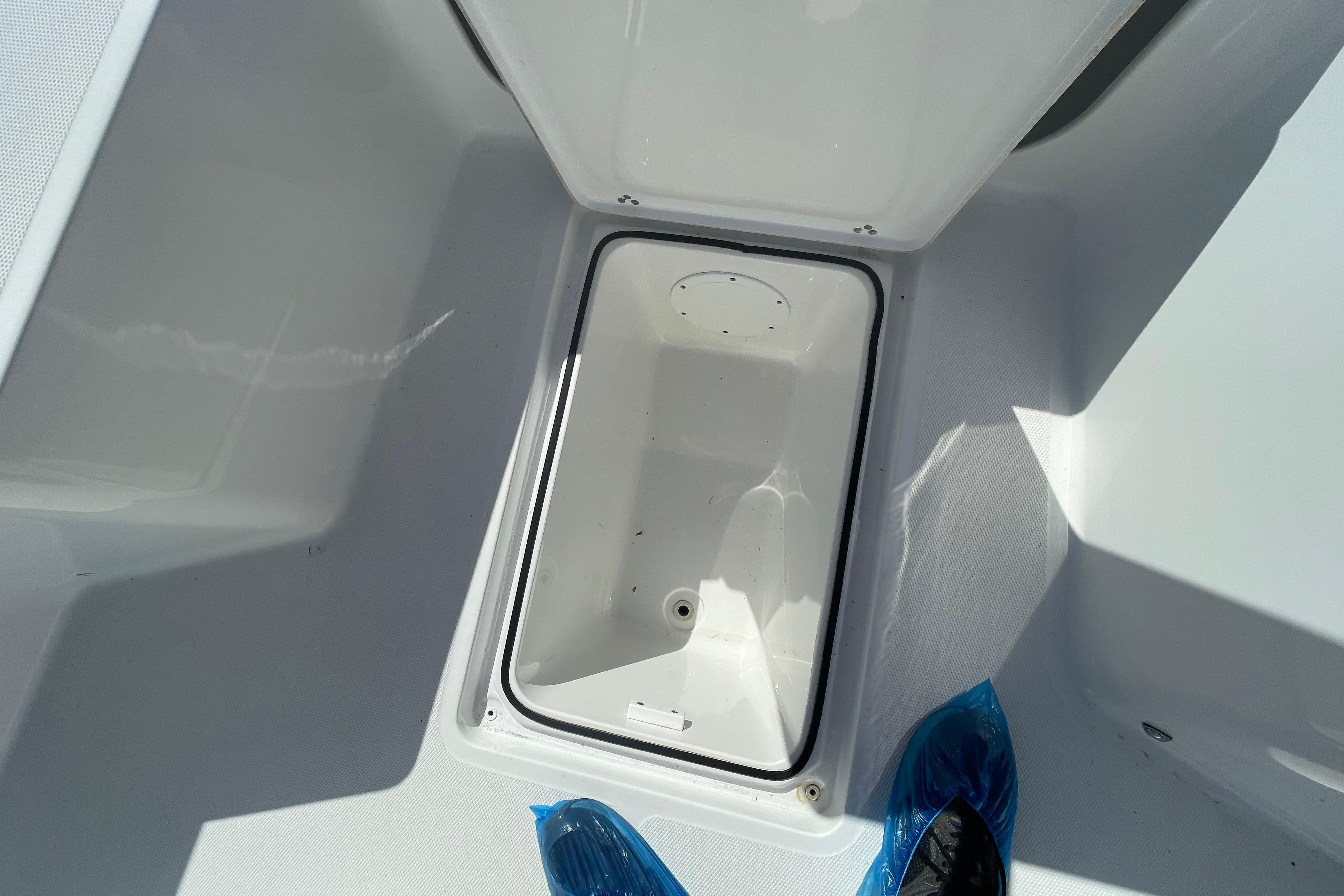 2022 Wellcraft 202 Fisherman storage compartment, open lid, white interior, blue shoe covers visible.