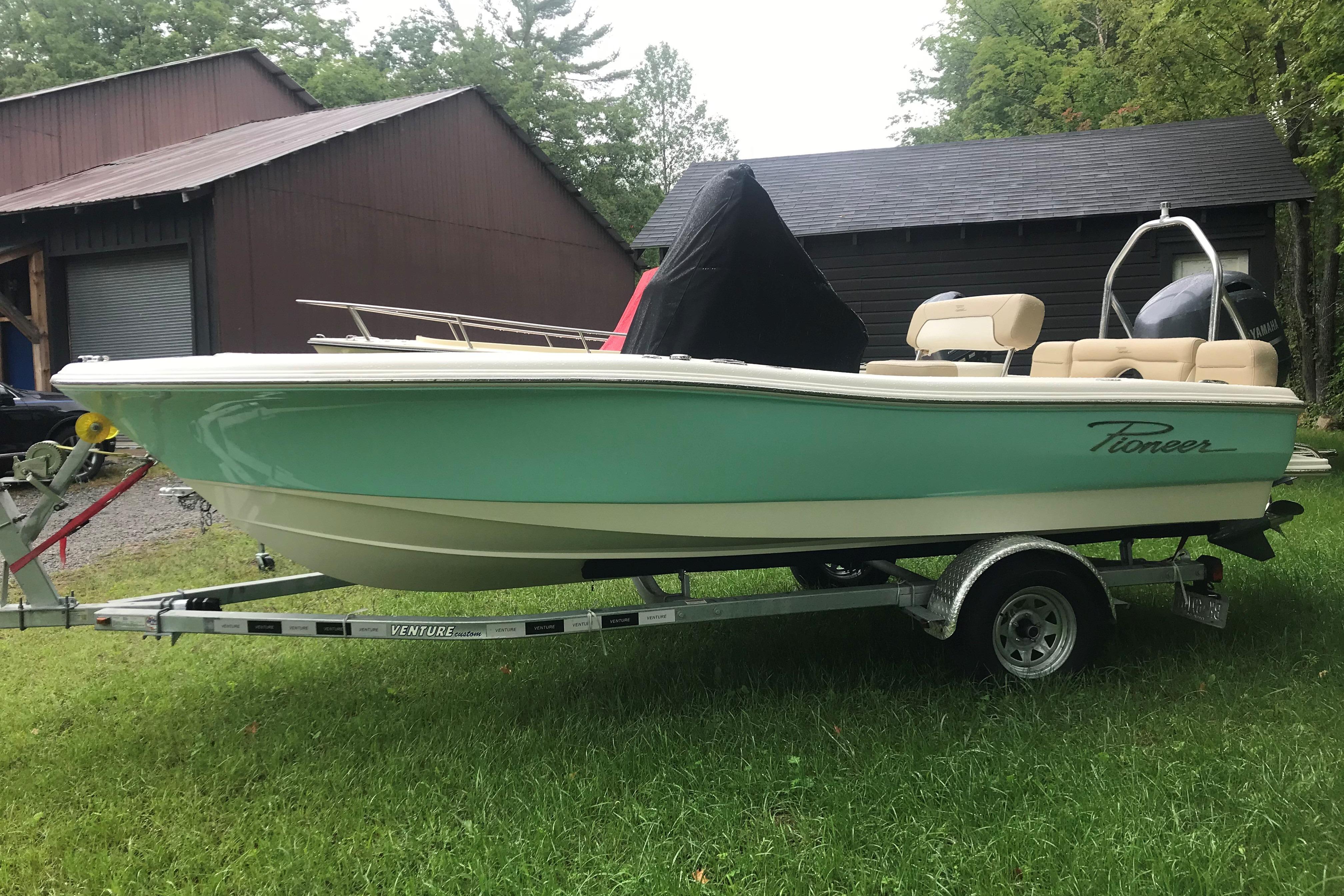 2026 Pioneer 180 Islander boat on trailer, parked on grass near a wooden building.