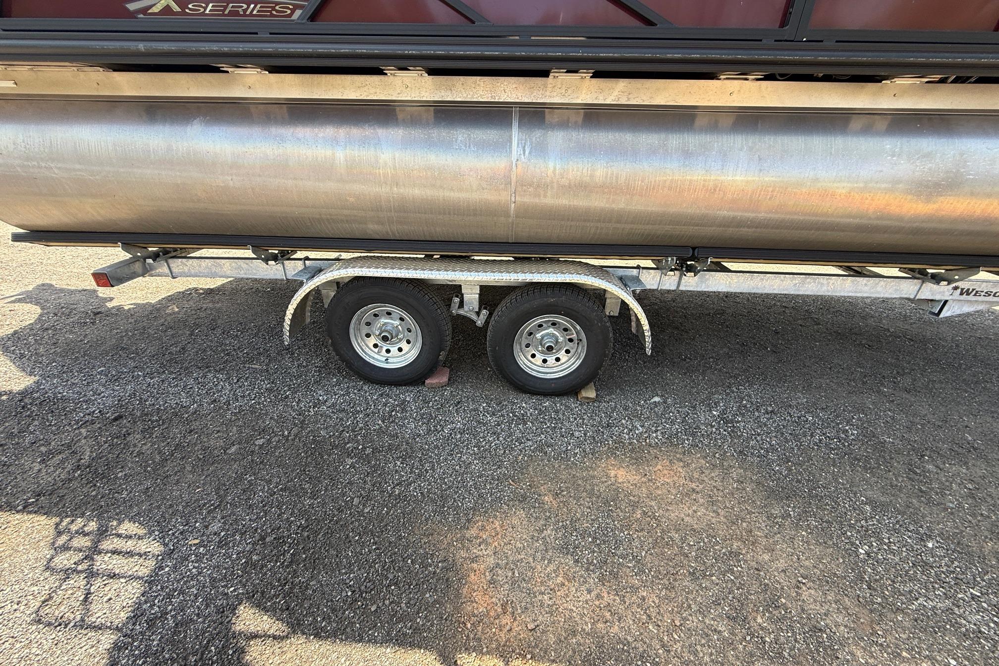 Trailer with dual wheels carrying a 2024 Sylvan X1 CLZ DH pontoon boat.