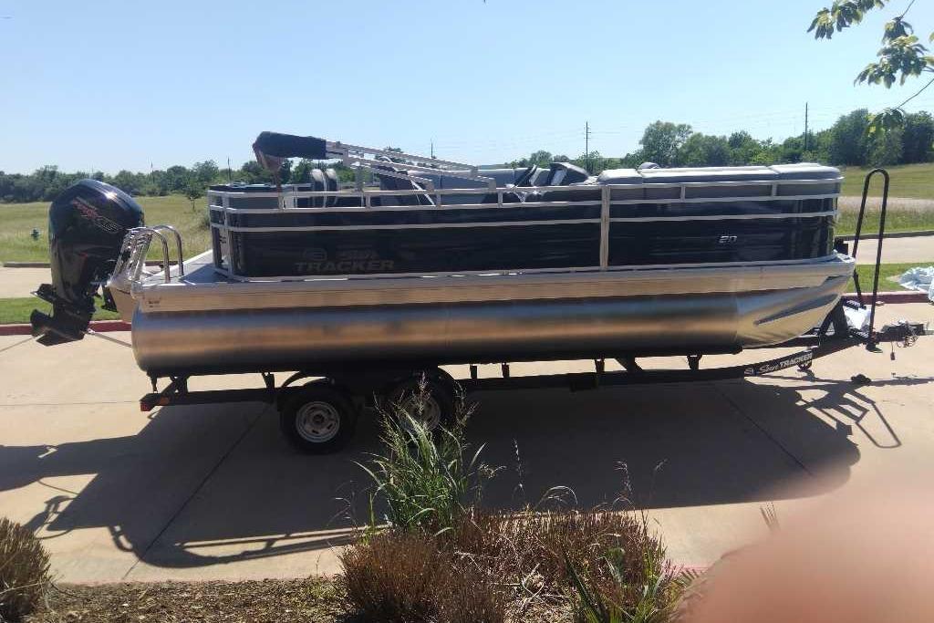 2026 Sun Tracker SportFish 20 DLX pontoon boat on trailer, parked outdoors.