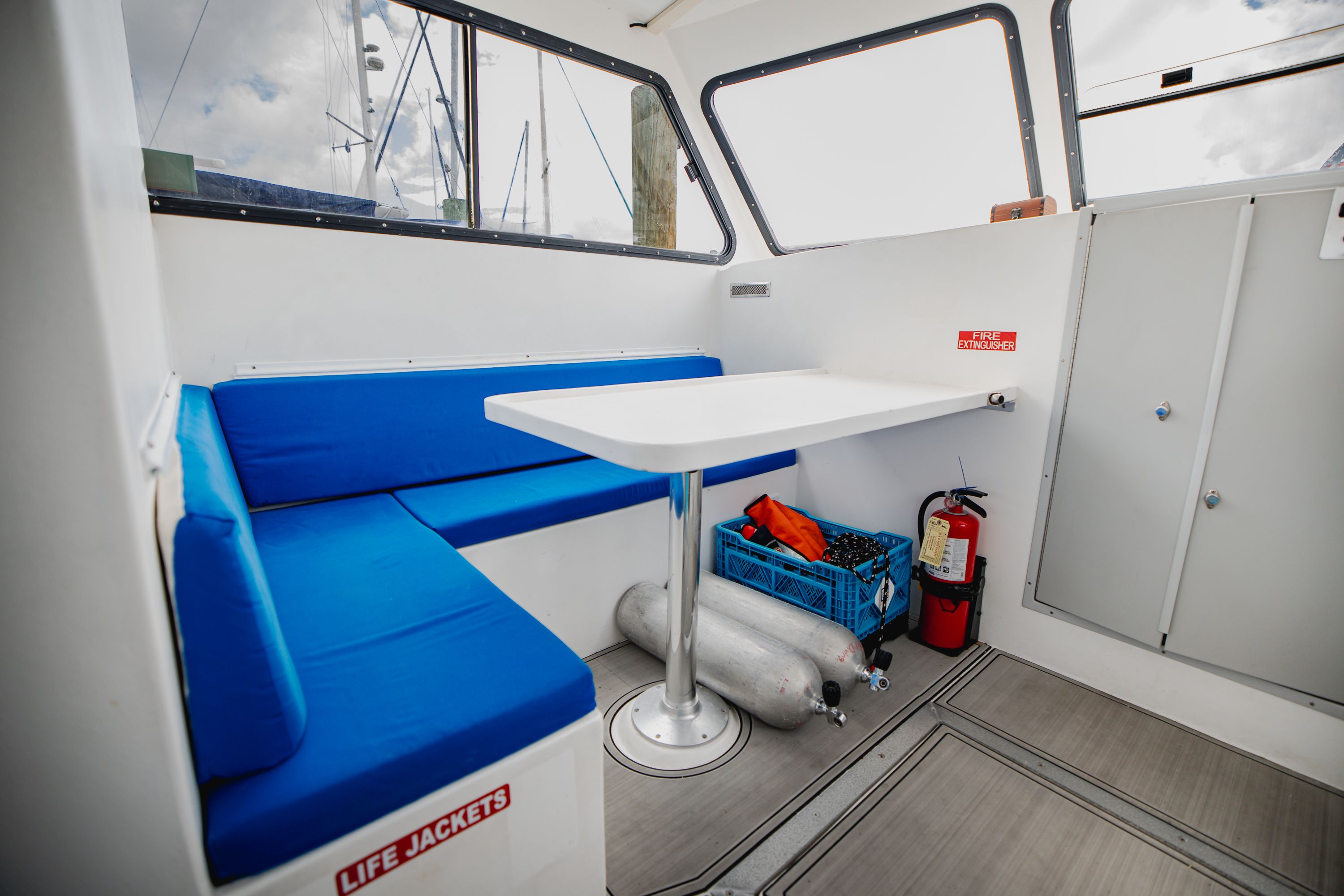 Interior of a dive boat with blue seating, table, fire extinguisher, and life jackets.