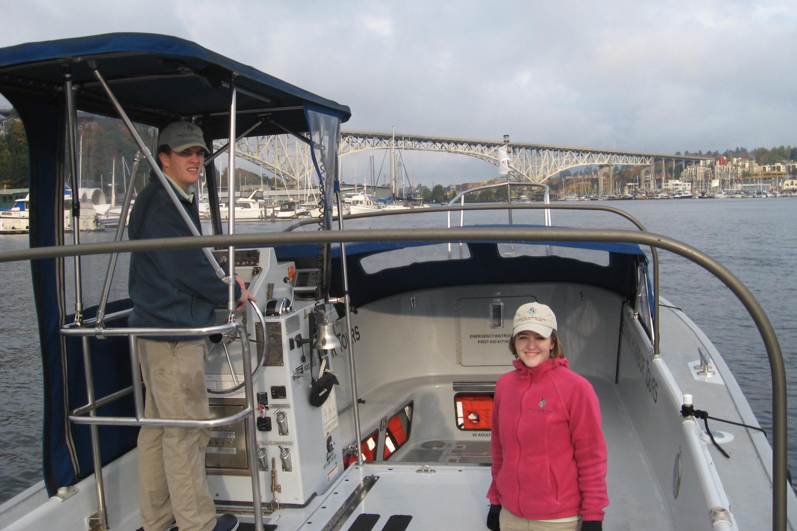Two people on a 1994 Willard US Navy boat, with a bridge in the background.