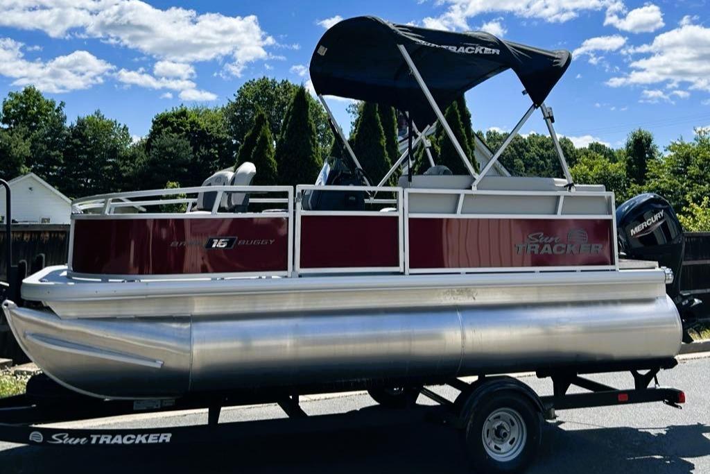2026 Sun Tracker Bass Buggy 16 XL Select pontoon boat on trailer, outdoors.