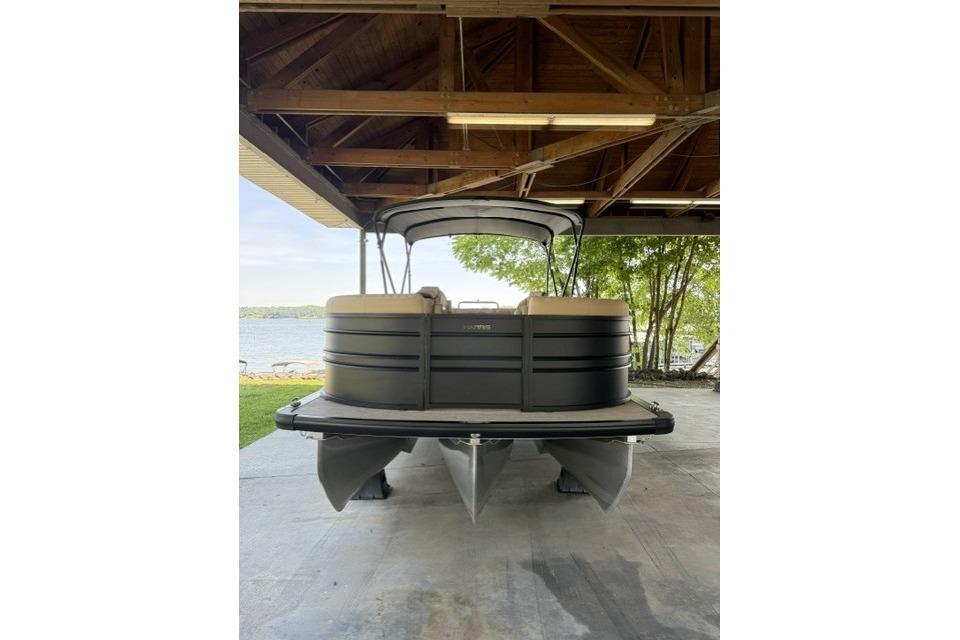 2025 Harris Sunliner 230 pontoon boat under a wooden shelter by a lake.