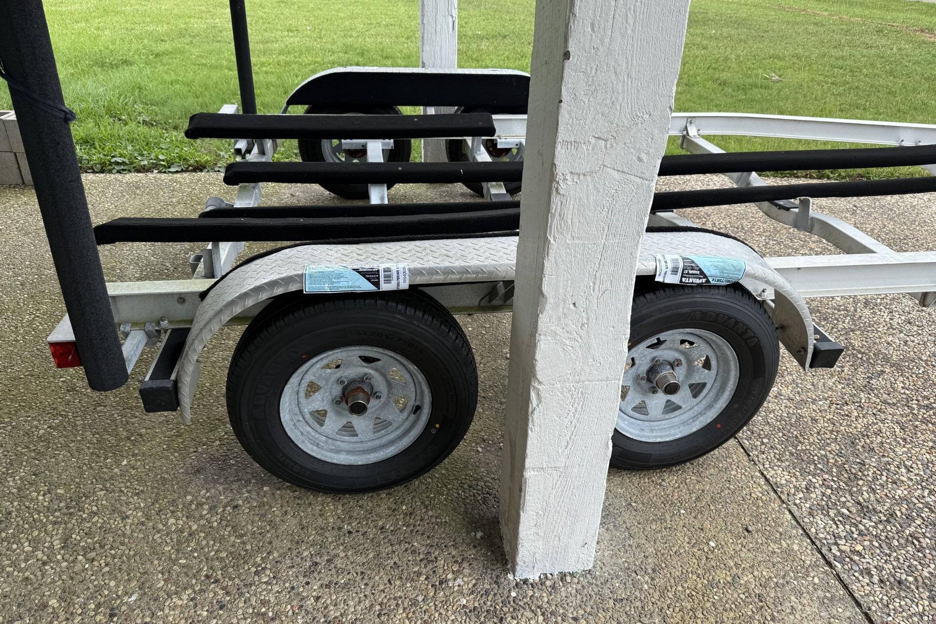 Boat trailer for 2017 Blue Wave 2200 PureBay, parked on gravel near grass.