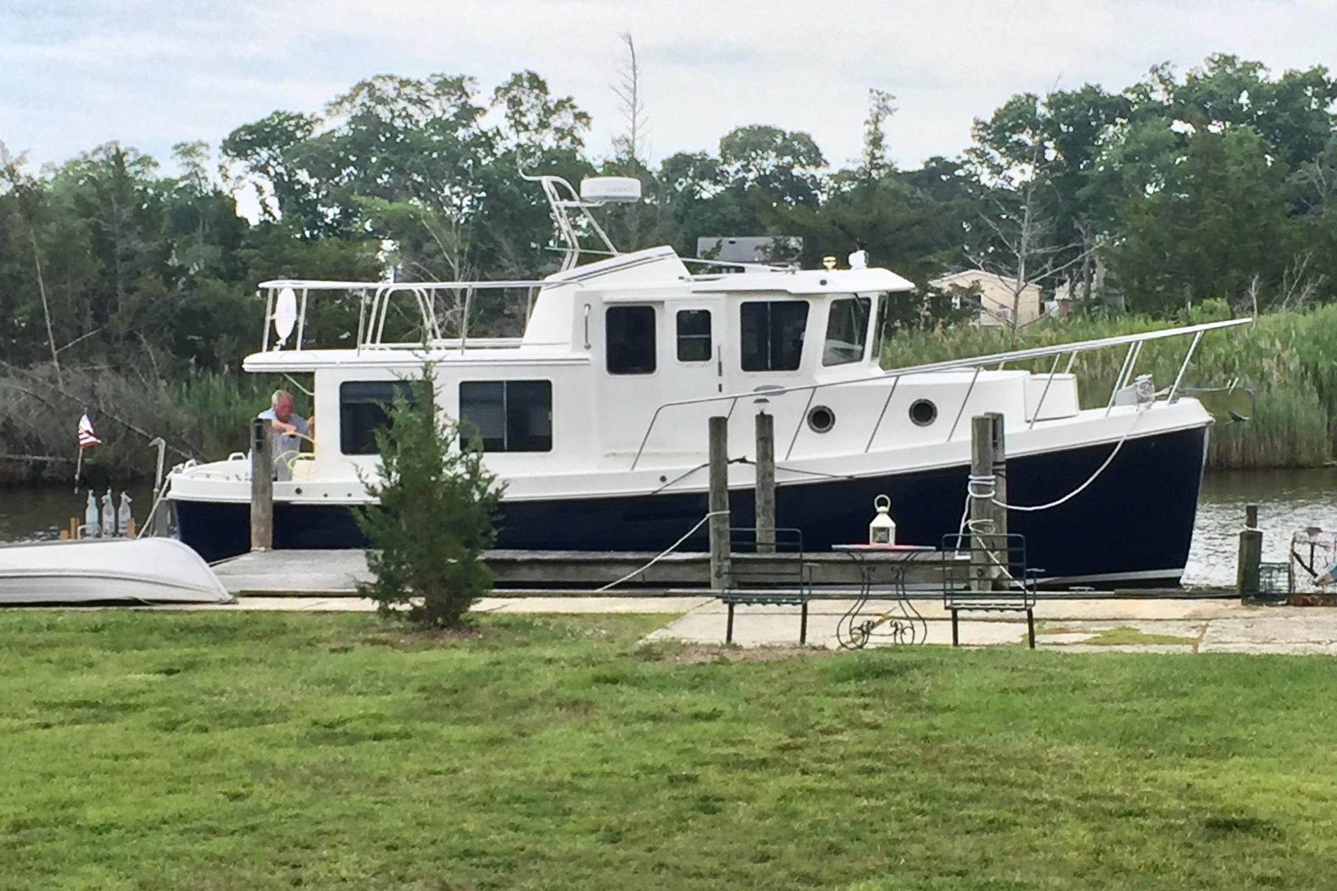 2010 American Tug "34" Pilothouse Trawler docked by a grassy shoreline.