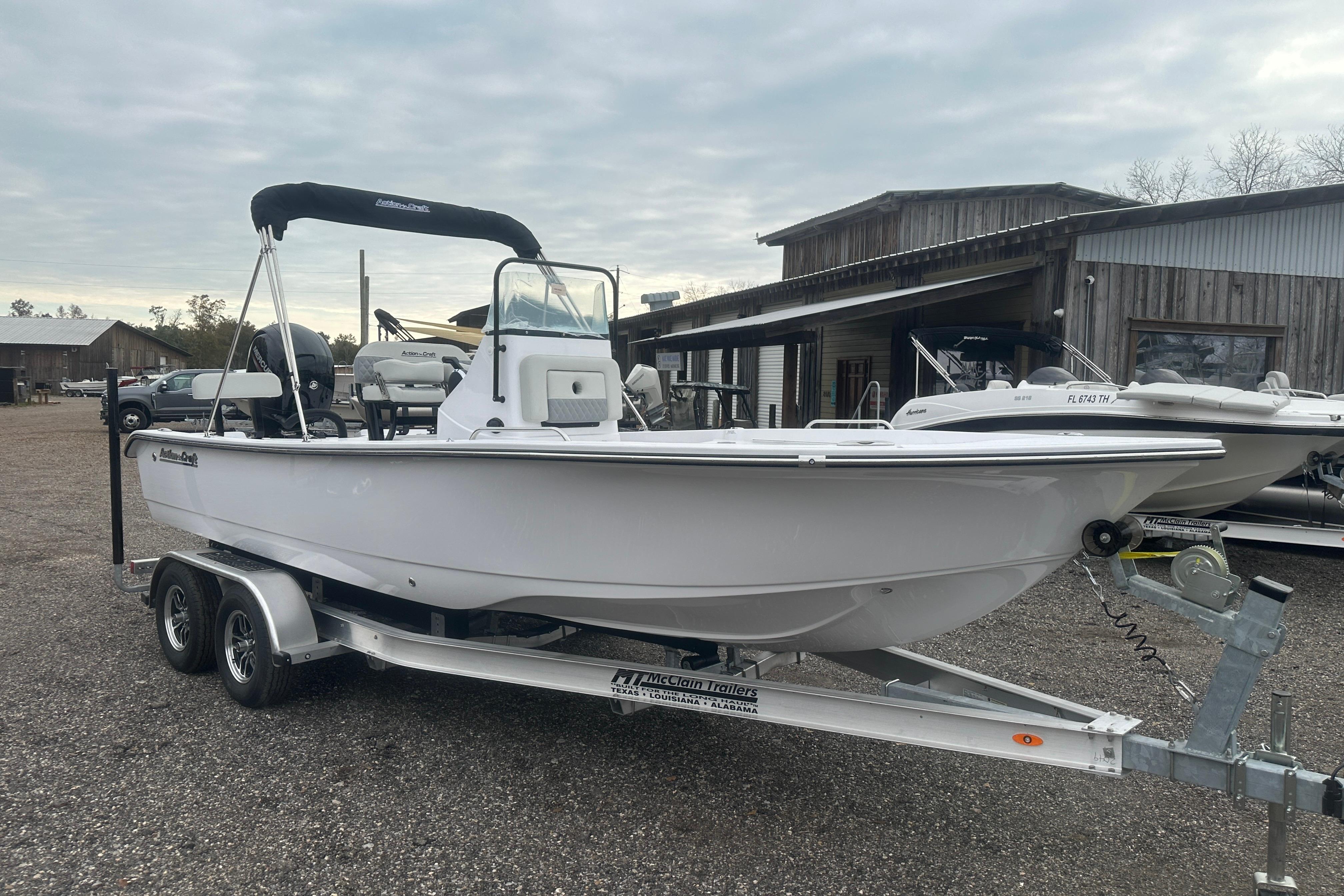 2026 Action Craft 22 Bay boat on trailer, parked outdoors near wooden buildings.