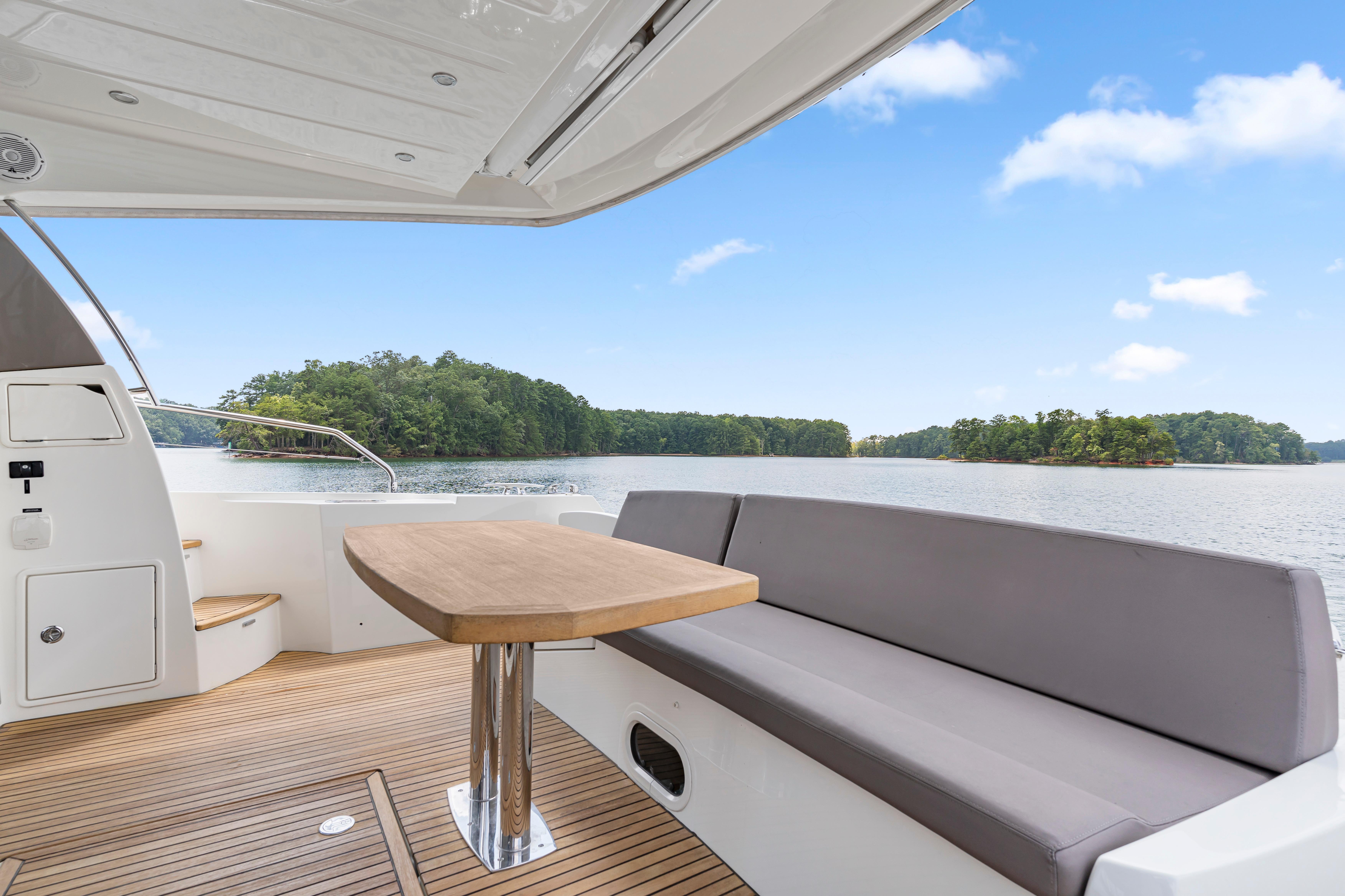Luxury yacht deck with seating and table, overlooking serene lake and lush greenery. Prestige 500, 2017.
